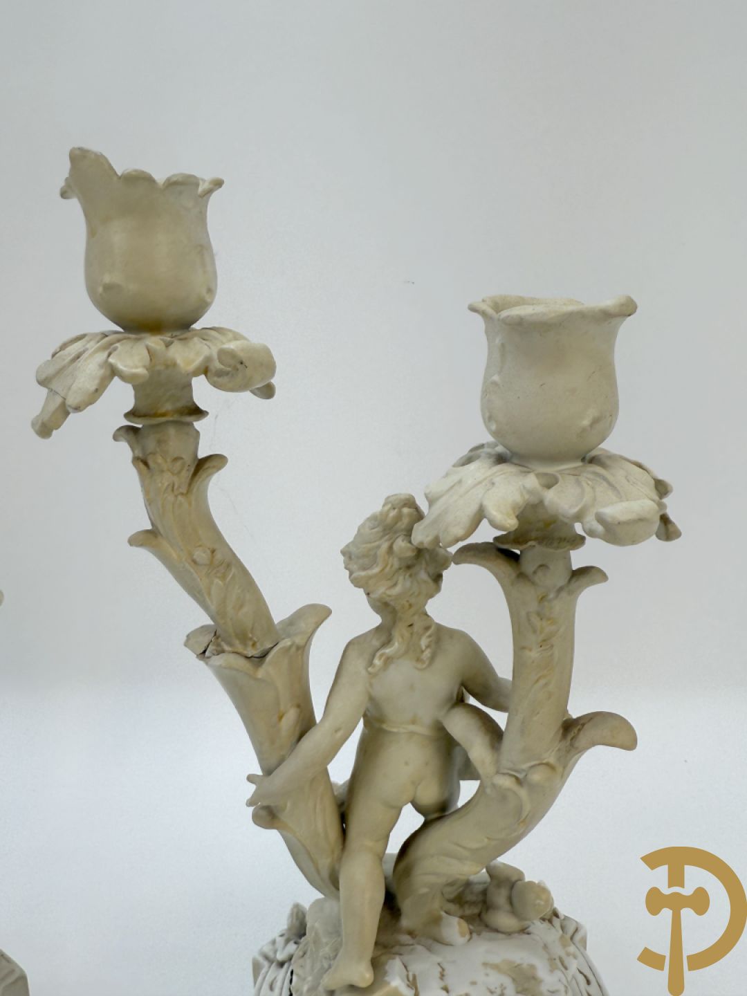 Driedelige porseleinen garnituur bestaande uit pendule bezet met lieftallig koppel, geflankeerd door paar kandelaars met cupido