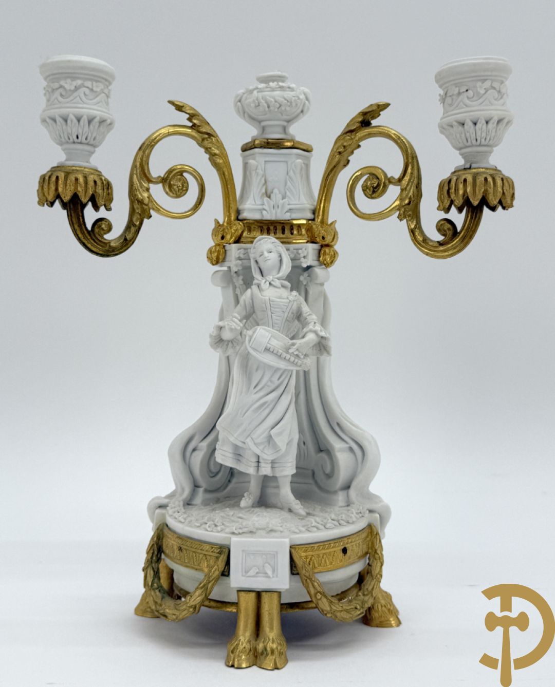 Driedelige porseleinen garnituur met bronsbeslag bestaande uit pendule met dame en amfoor geflankeerd door paar kandelaars bezet met personages