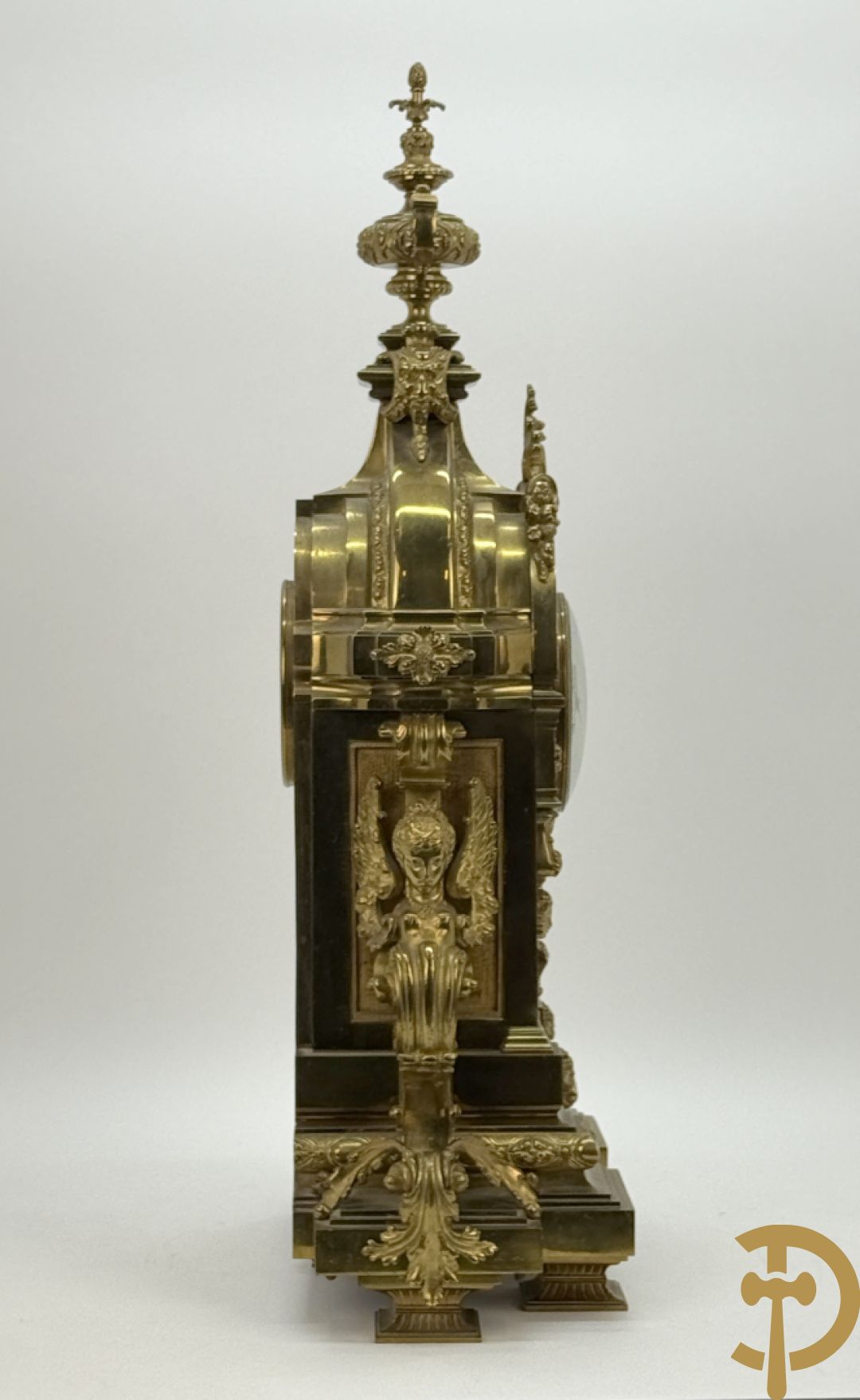 Vuurvergulde bronzen pendule, zijdelings bezet met gevleugelde dames, bovenaan met amfoor