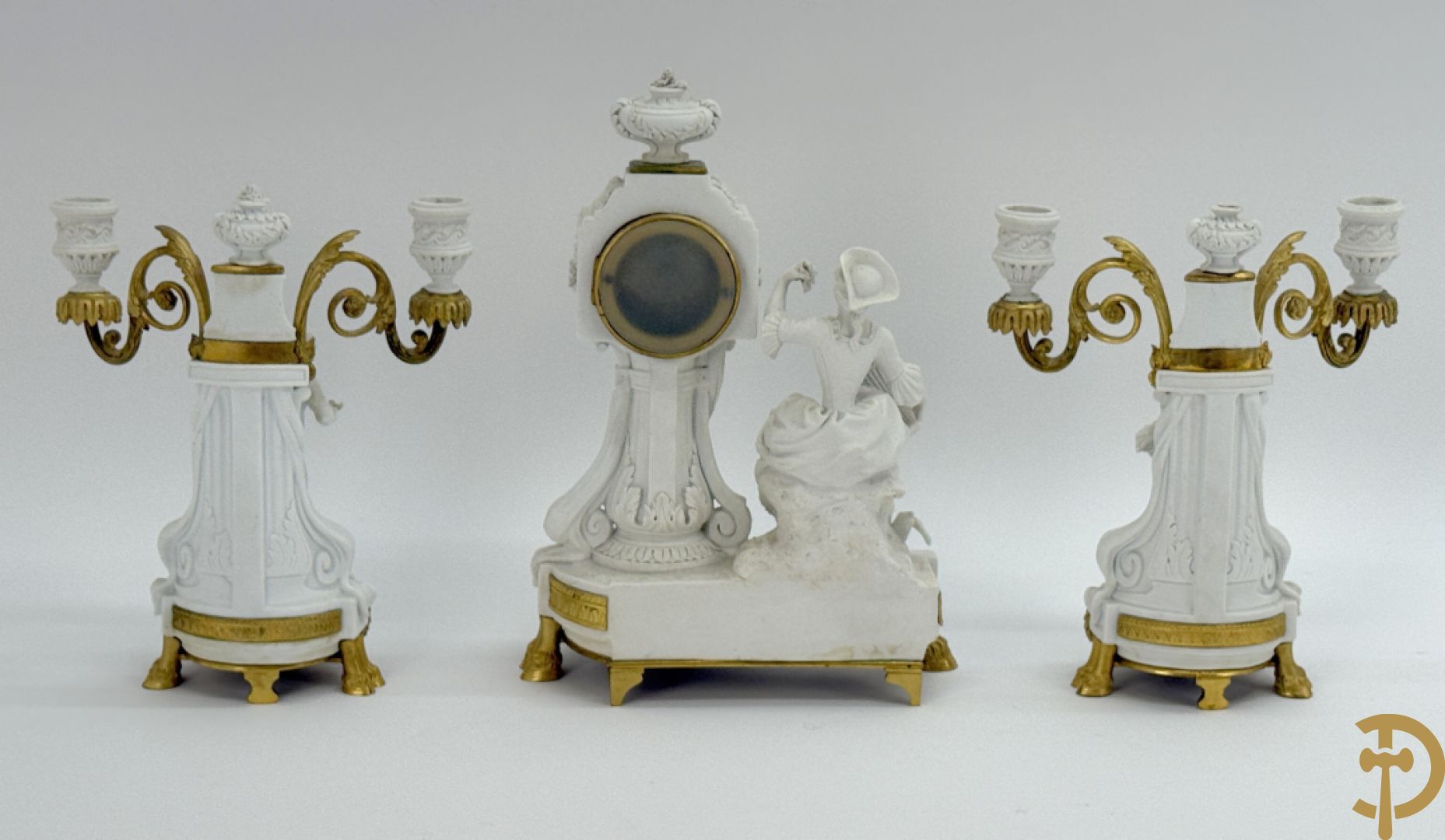 Driedelige porseleinen garnituur met bronsbeslag bestaande uit pendule met dame en amfoor geflankeerd door paar kandelaars bezet met personages