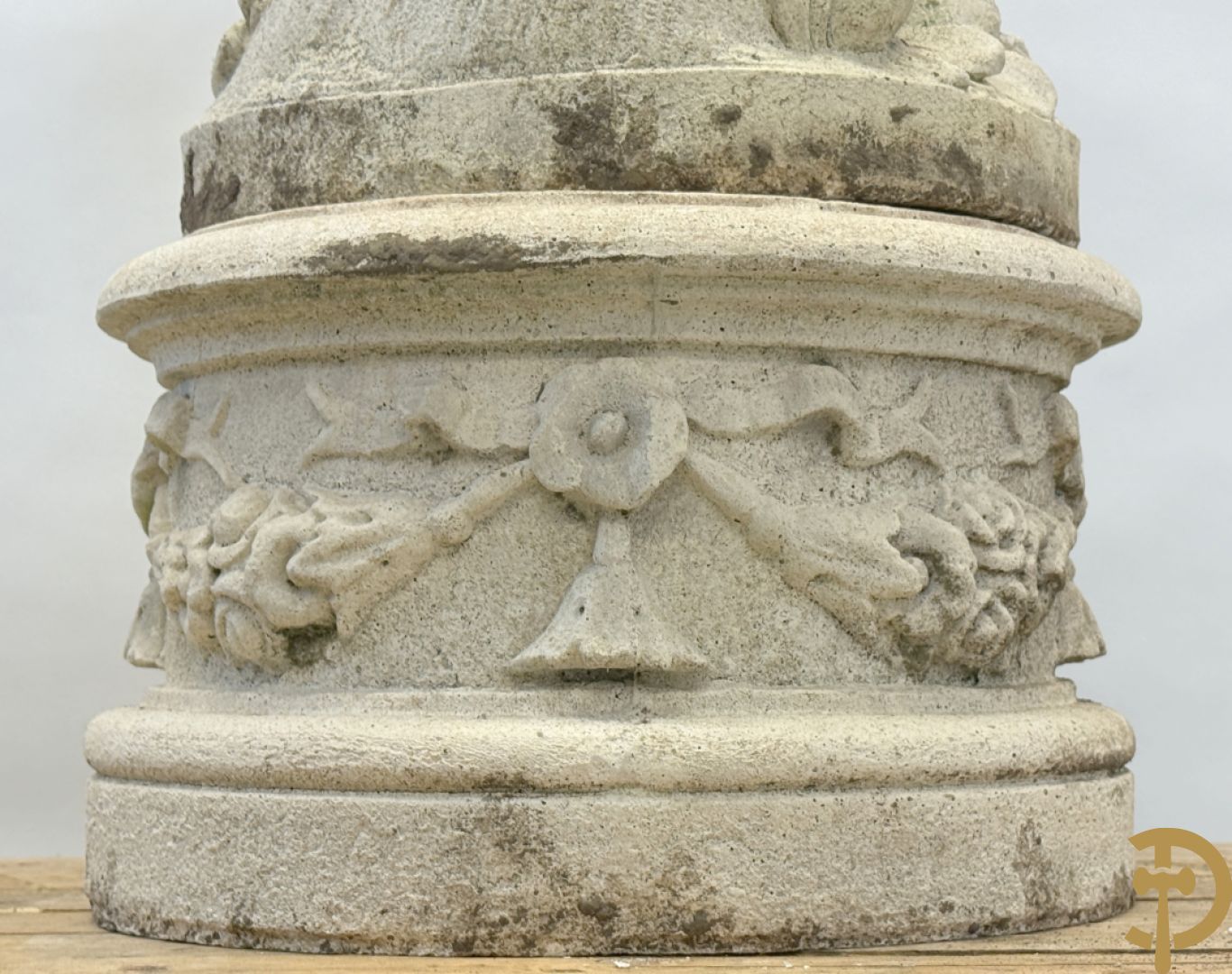 Stenen tuinbeeld van jongeman met mand in de hand op sokkel met guirlandes