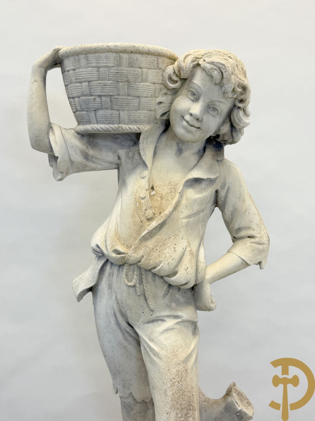 Stenen tuinbeeld van jongeman met mand in de hand op sokkel met guirlandes