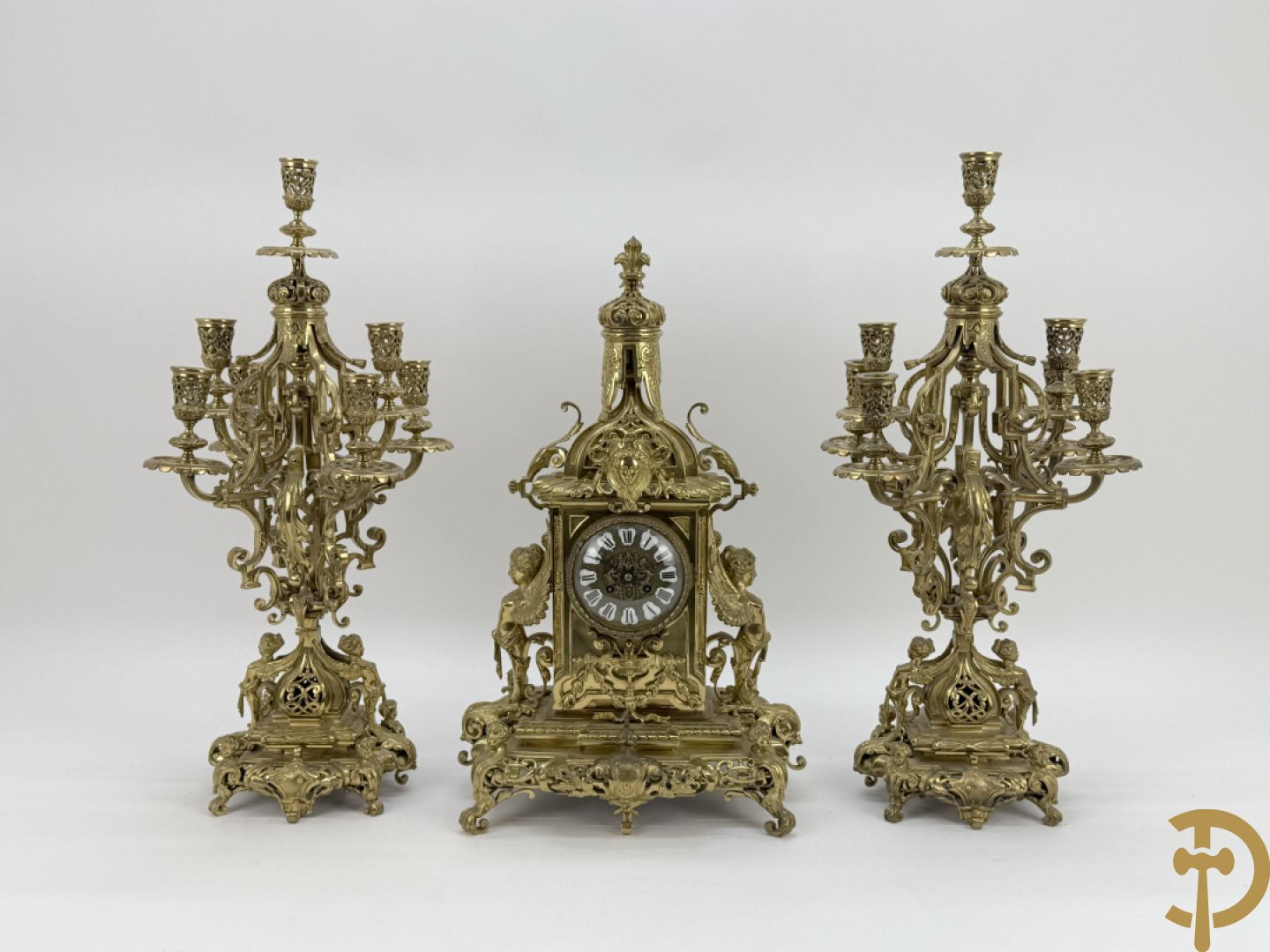 Driedelige bronzen vergulde garntiuur bestaande uit klok met medusahoofden en sfinxen, geflankeerd door paar zevenarmige kandelaars met accanthusranken en sfinxen