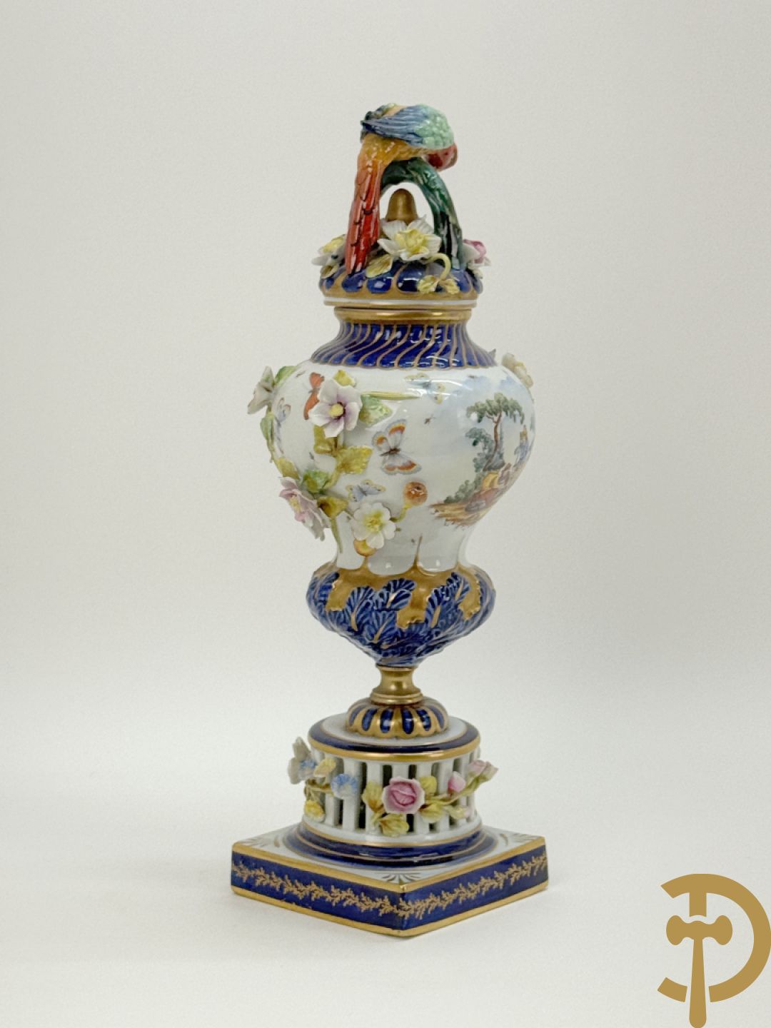 Porseleinen siervaas met handbeschilderd geanimeerd decor bezet met basrelief van bloemen en bovenaan bekroond met deksel met vogel