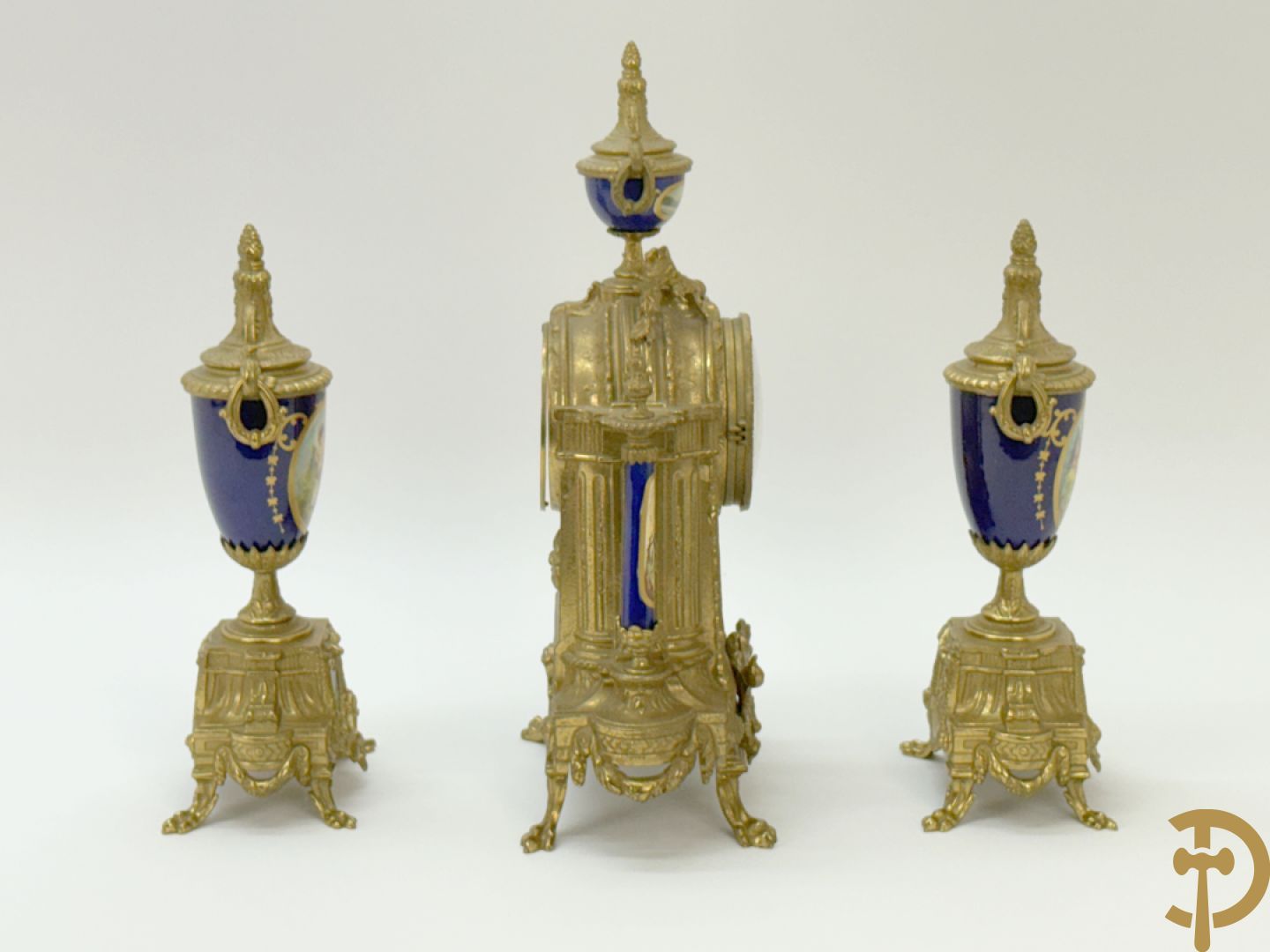 Driedelige koperen garnituur bestaande uit pendule met beschilderd romantisch tafereel en amfoor, zijdelings bezet met paar cassolettes met geanimeerde scènes, onleesbaar getekend rechts onder klok