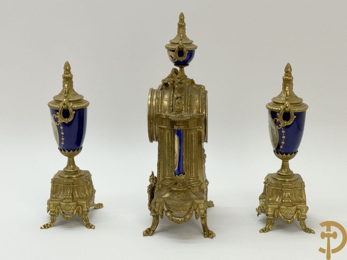 Driedelige koperen garnituur bestaande uit pendule met beschilderd romantisch tafereel en amfoor, zijdelings bezet met paar cassolettes met geanimeerde scènes, onleesbaar getekend rechts onder klok