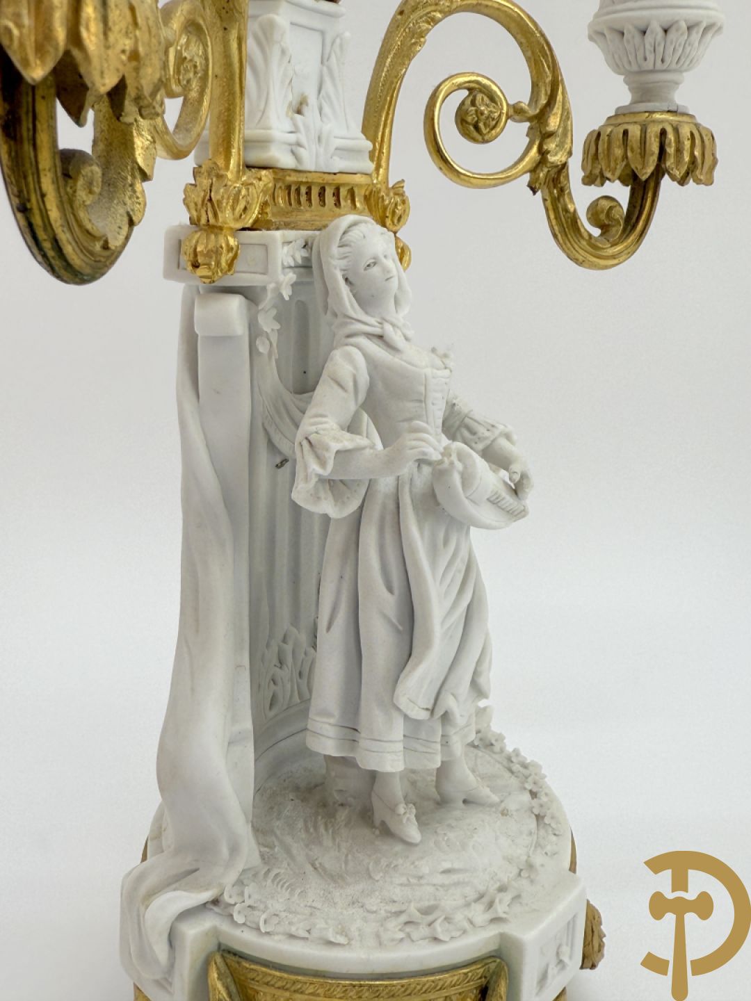 Driedelige porseleinen garnituur met bronsbeslag bestaande uit pendule met dame en amfoor geflankeerd door paar kandelaars bezet met personages