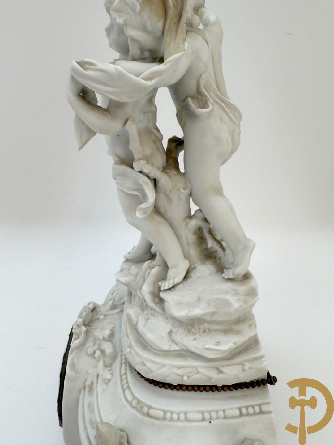 Driedelige porseleinen garnituur bestaande uit pendule bezet met lieftallig koppel, geflankeerd door paar kandelaars met cupido