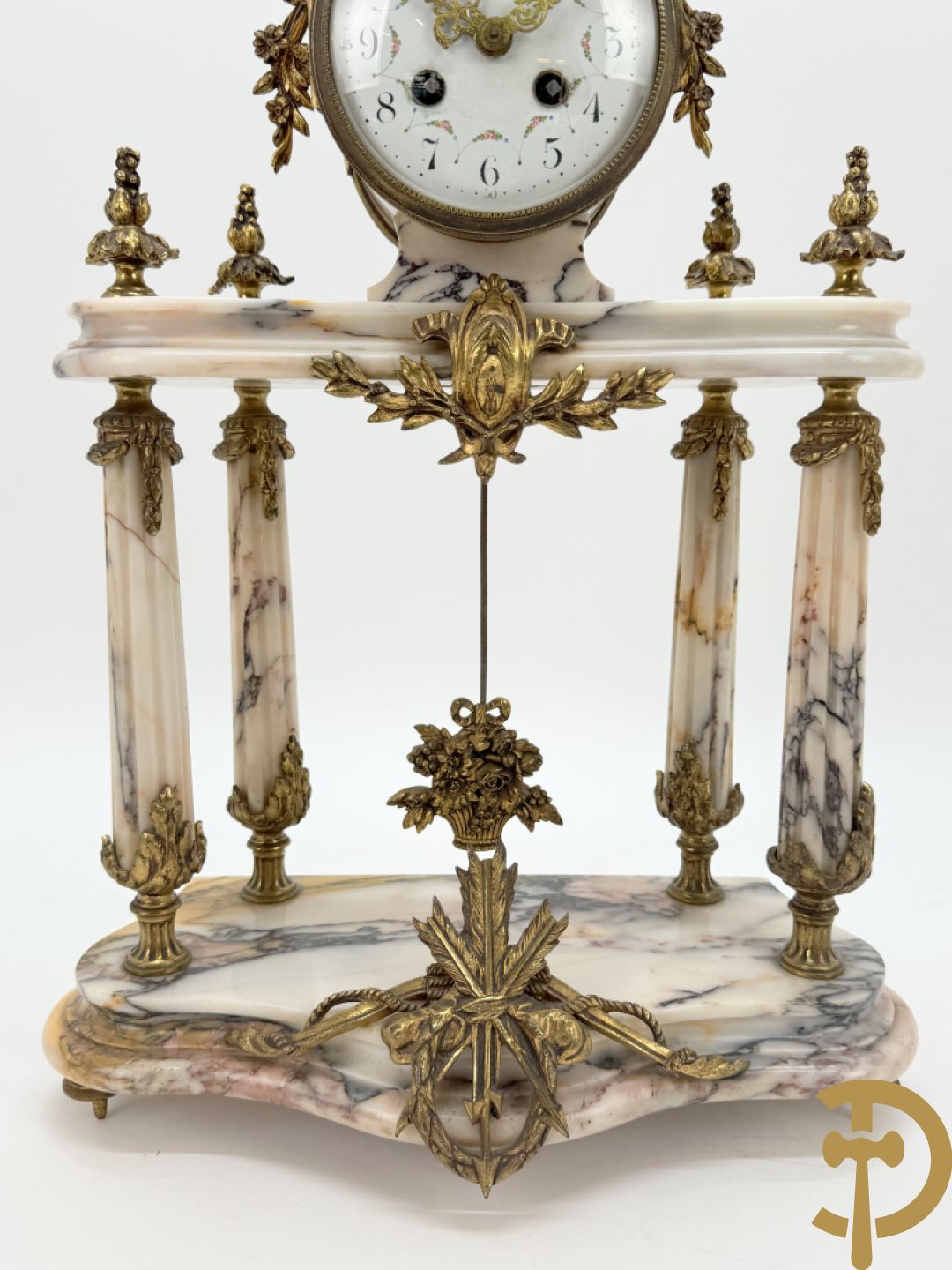 Driedelige wit marmeren garnituur bestaande uit vierzuilenpendule met bloemen en troffee geflankeerd door paar cassolettes met ramskoppen bezet