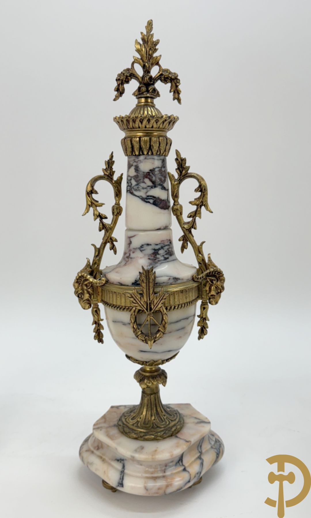 Driedelige wit marmeren garnituur bestaande uit vierzuilenpendule met bloemen en troffee geflankeerd door paar cassolettes met ramskoppen bezet