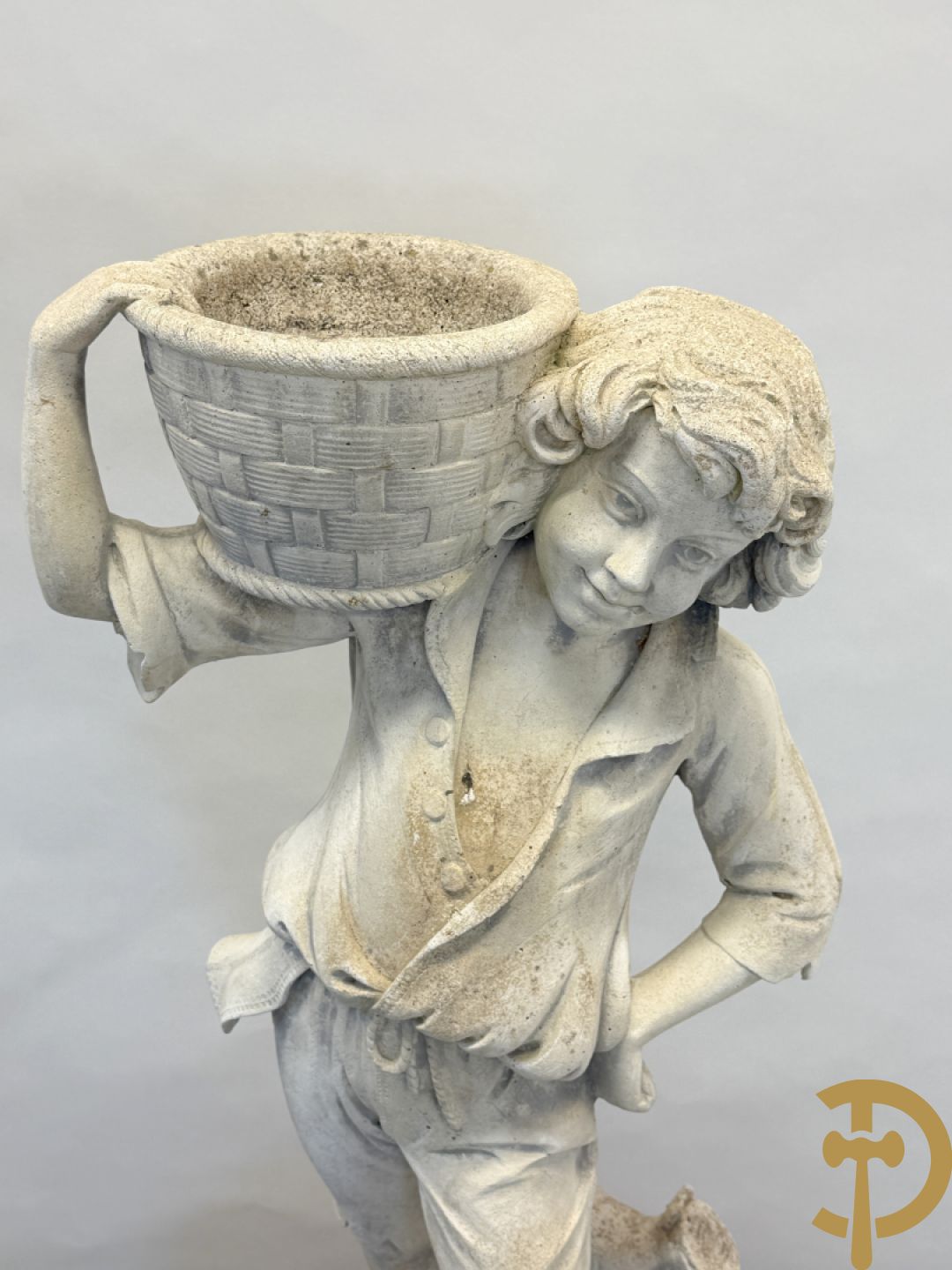 Stenen tuinbeeld van jongeman met mand in de hand op sokkel met guirlandes