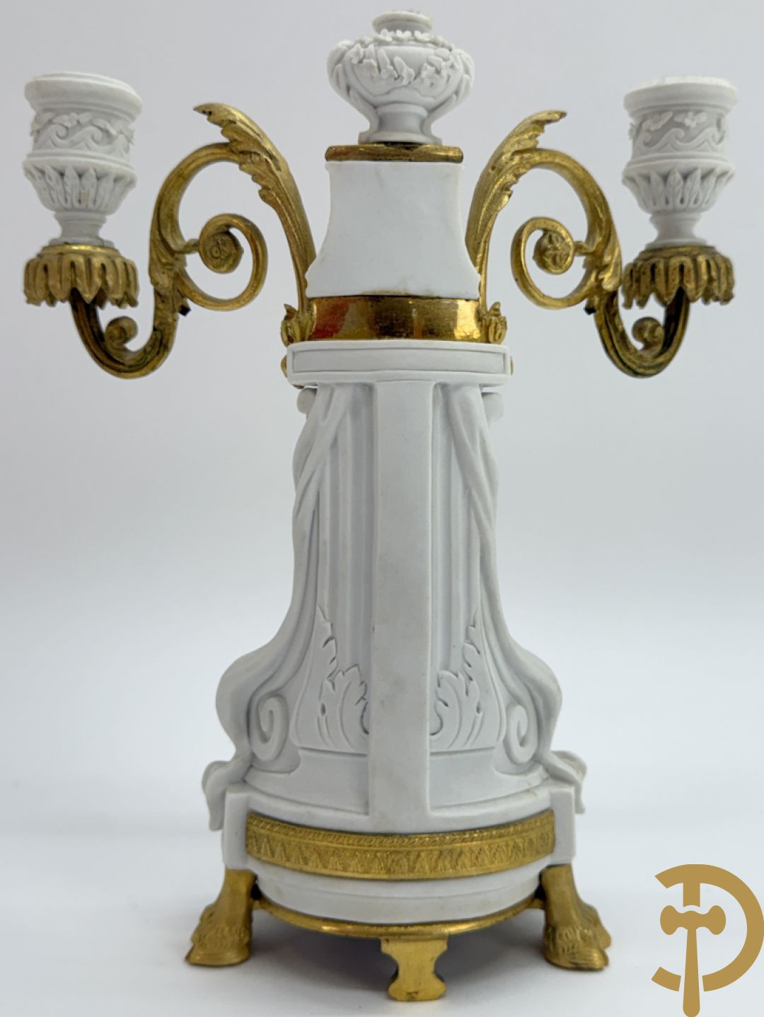 Driedelige porseleinen garnituur met bronsbeslag bestaande uit pendule met dame en amfoor geflankeerd door paar kandelaars bezet met personages