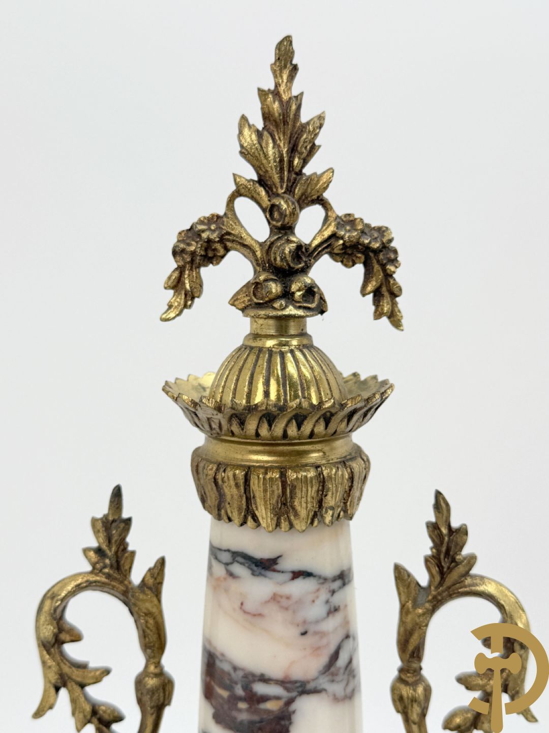 Driedelige wit marmeren garnituur bestaande uit vierzuilenpendule met bloemen en troffee geflankeerd door paar cassolettes met ramskoppen bezet