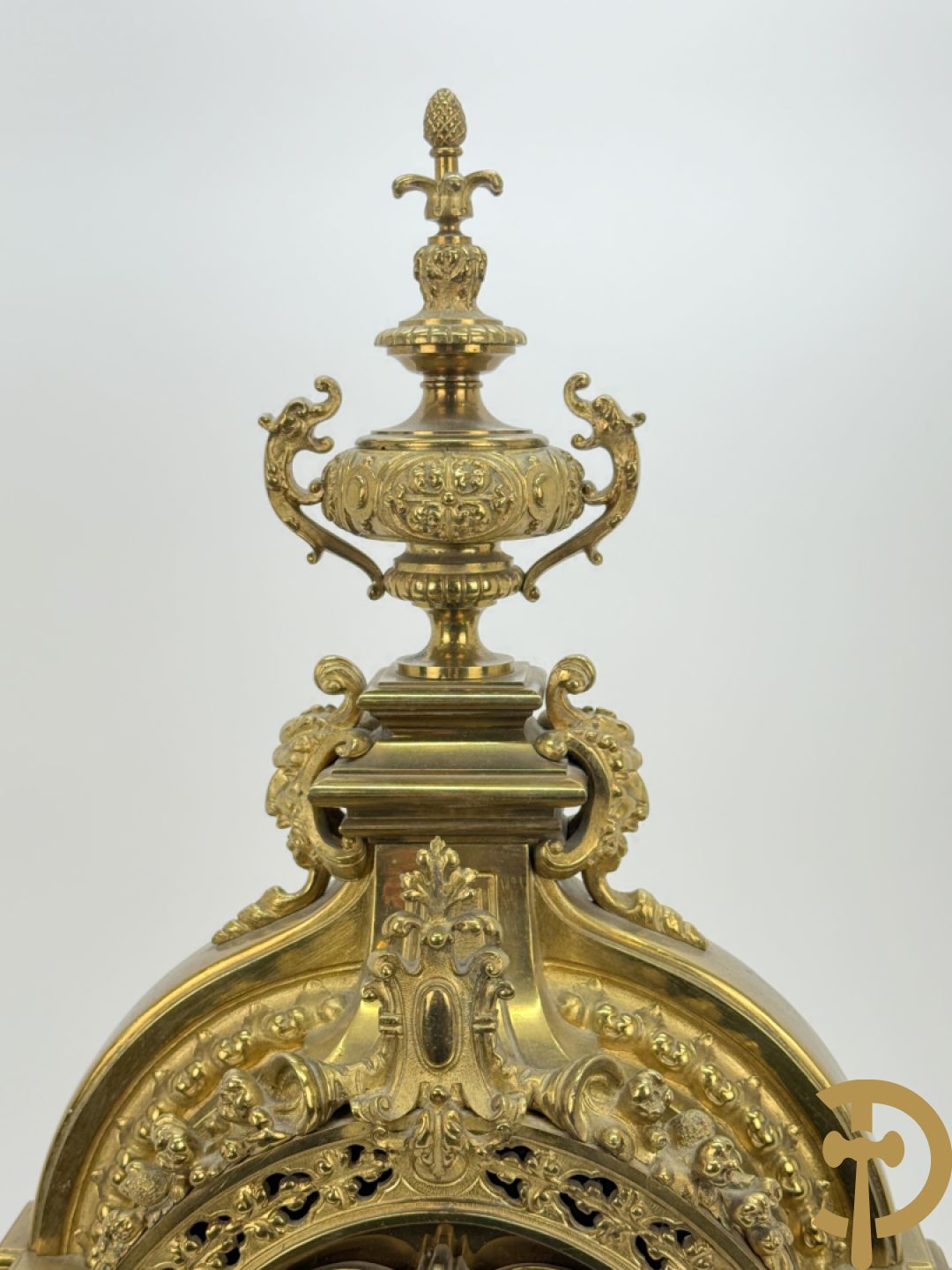 Vuurvergulde bronzen pendule, zijdelings bezet met gevleugelde dames, bovenaan met amfoor