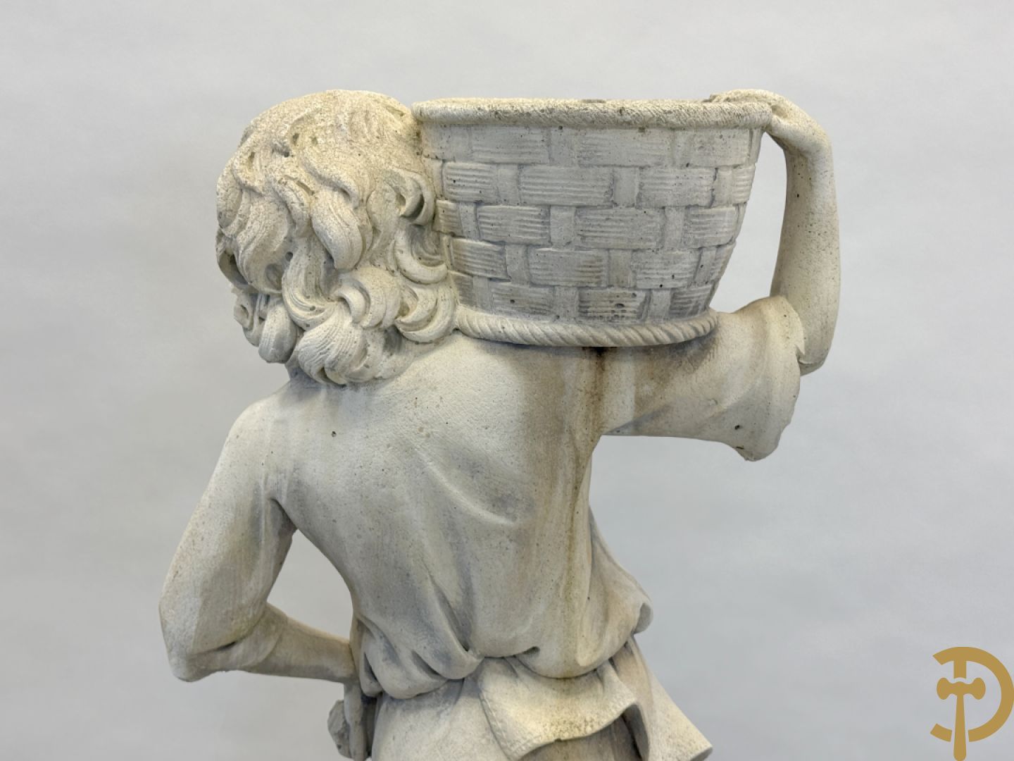 Stenen tuinbeeld van jongeman met mand in de hand op sokkel met guirlandes