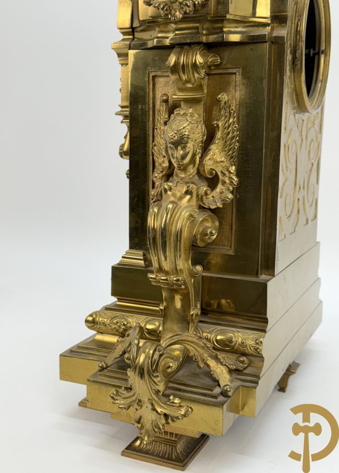 Vuurvergulde bronzen pendule, zijdelings bezet met gevleugelde dames, bovenaan met amfoor