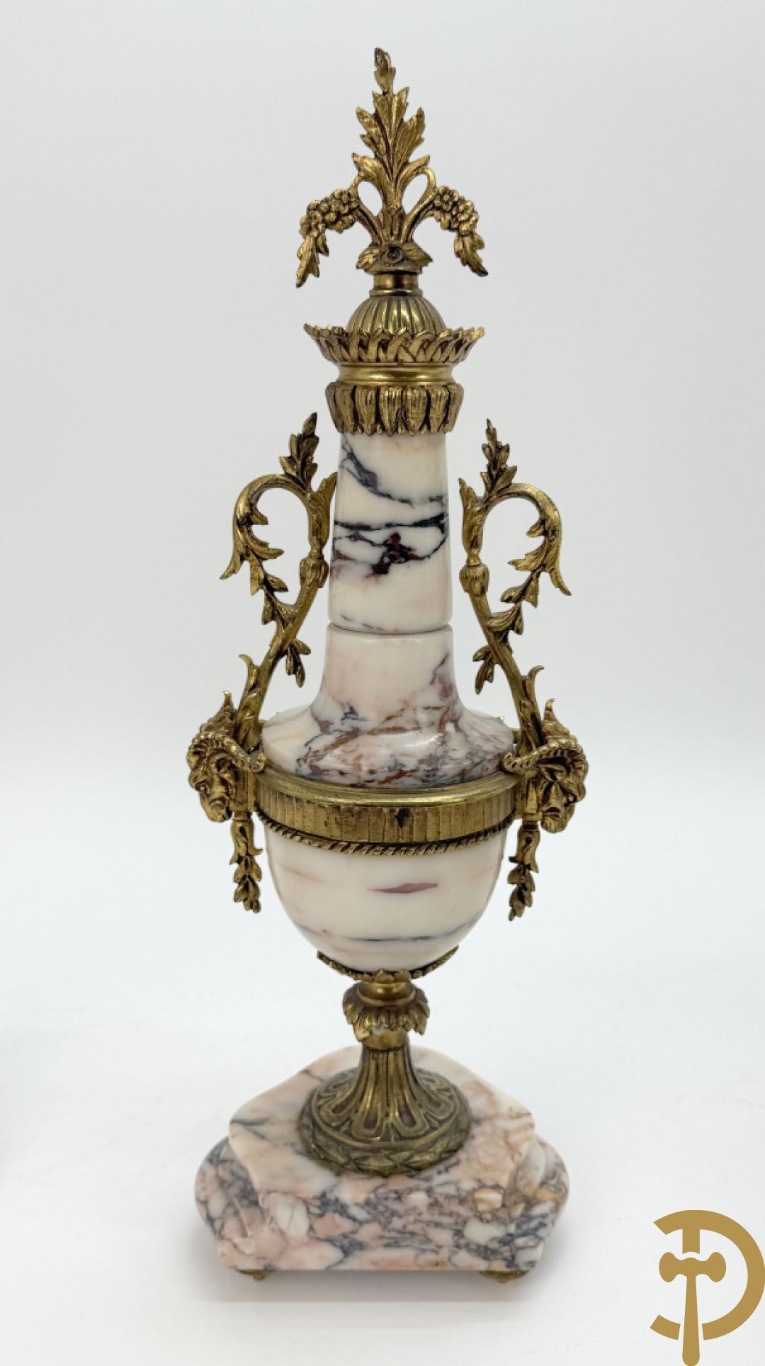 Driedelige wit marmeren garnituur bestaande uit vierzuilenpendule met bloemen en troffee geflankeerd door paar cassolettes met ramskoppen bezet