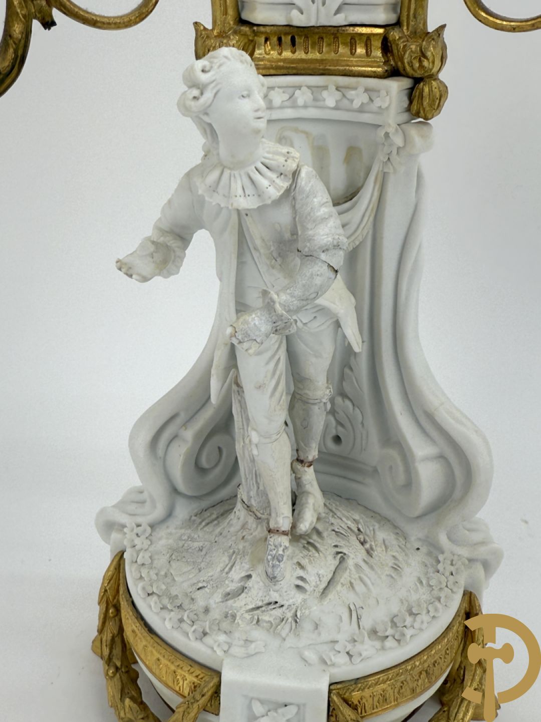 Driedelige porseleinen garnituur met bronsbeslag bestaande uit pendule met dame en amfoor geflankeerd door paar kandelaars bezet met personages