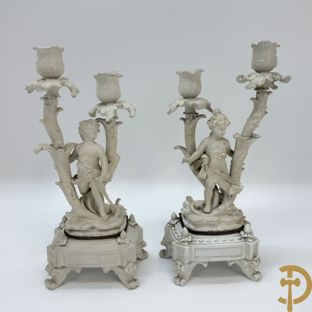 Driedelige porseleinen garnituur bestaande uit pendule bezet met lieftallig koppel, geflankeerd door paar kandelaars met cupido