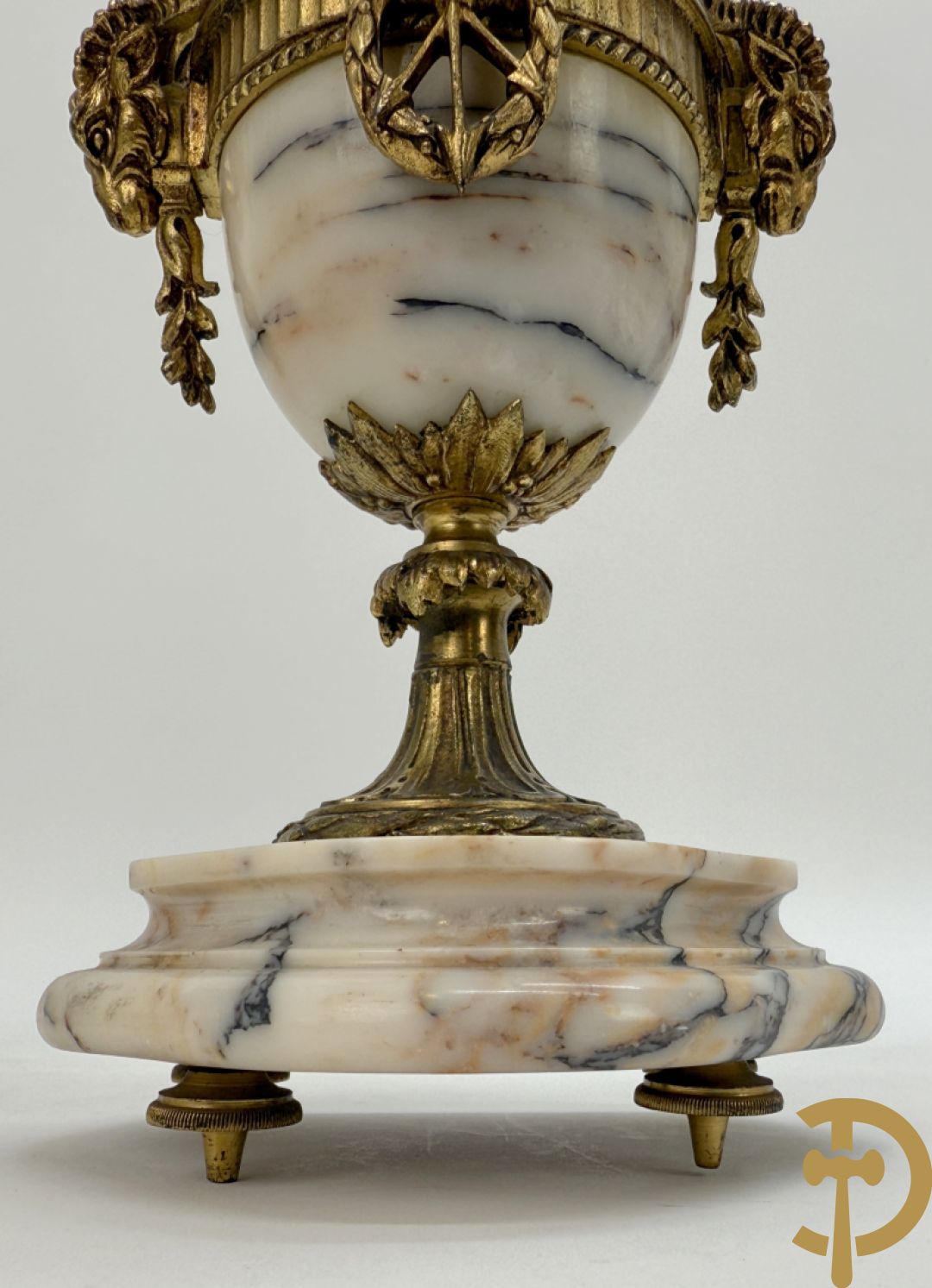 Driedelige wit marmeren garnituur bestaande uit vierzuilenpendule met bloemen en troffee geflankeerd door paar cassolettes met ramskoppen bezet