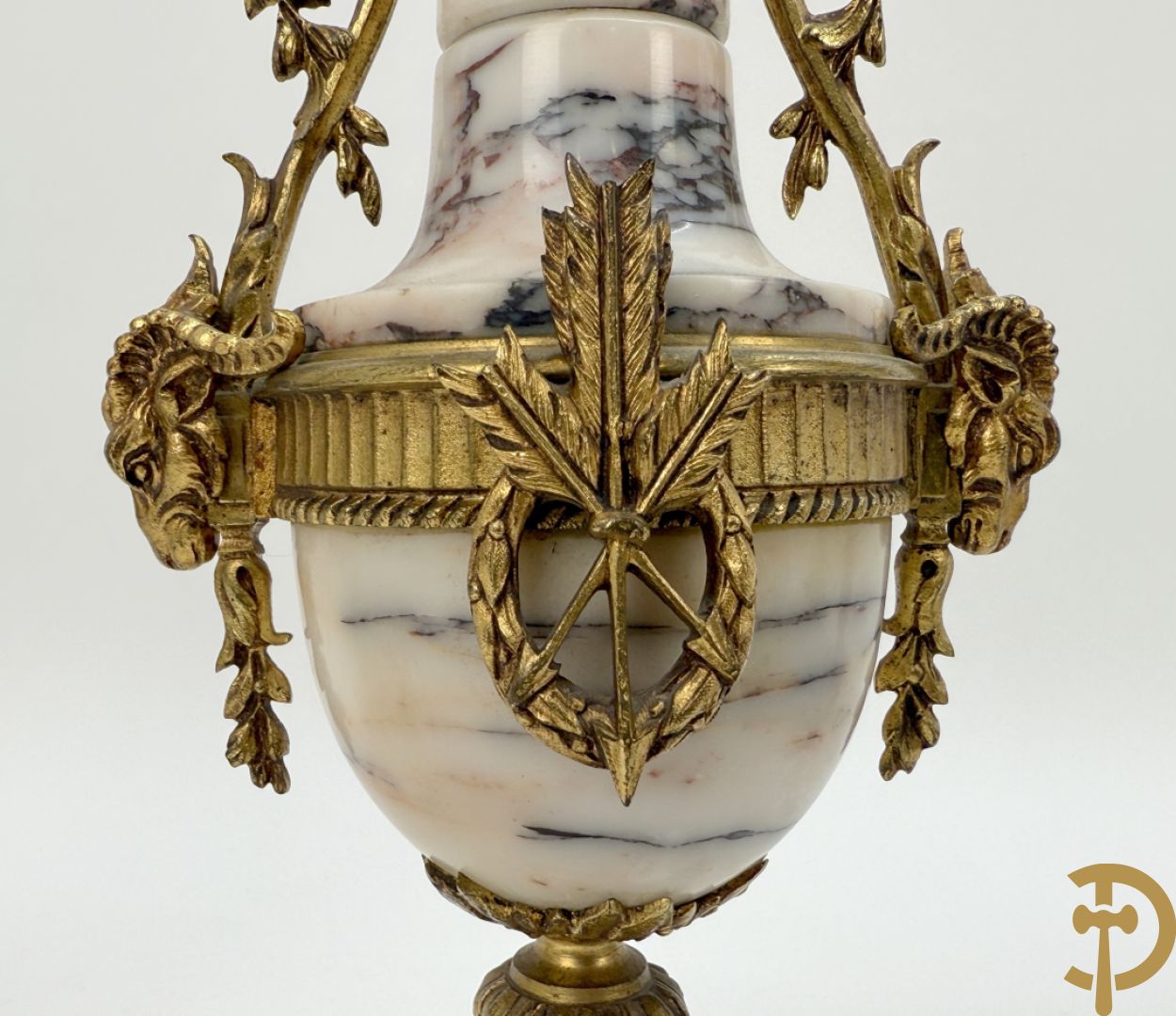 Driedelige wit marmeren garnituur bestaande uit vierzuilenpendule met bloemen en troffee geflankeerd door paar cassolettes met ramskoppen bezet