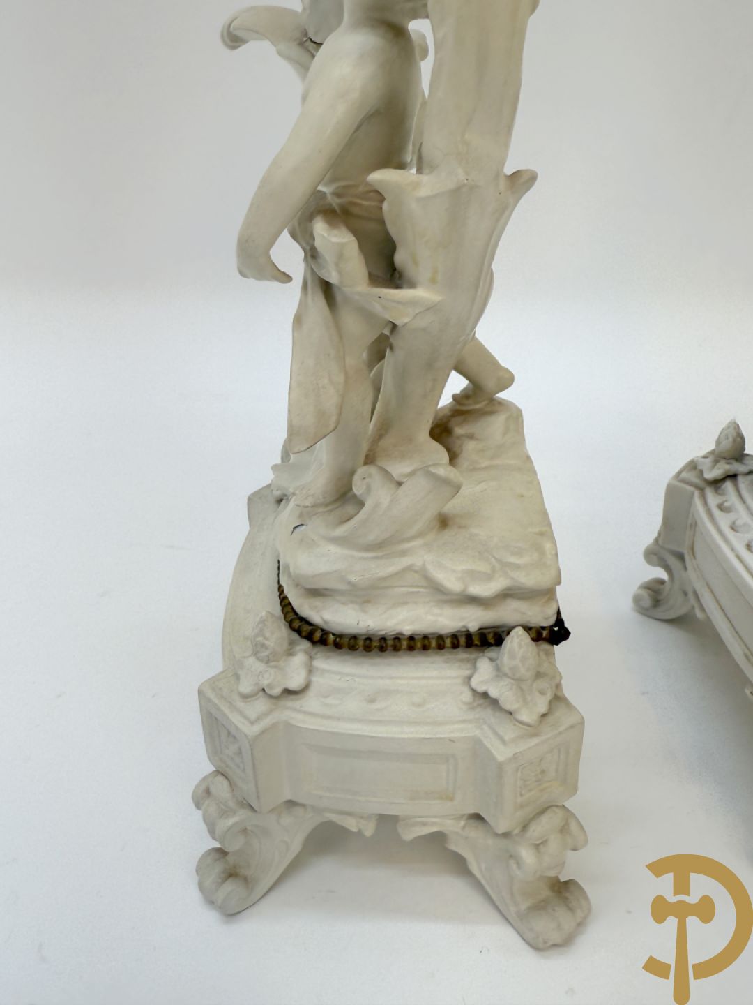 Driedelige porseleinen garnituur bestaande uit pendule bezet met lieftallig koppel, geflankeerd door paar kandelaars met cupido