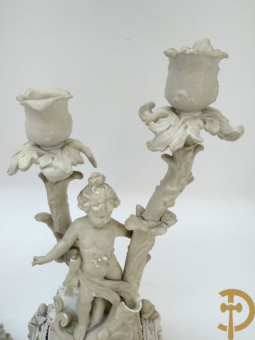 Driedelige porseleinen garnituur bestaande uit pendule bezet met lieftallig koppel, geflankeerd door paar kandelaars met cupido