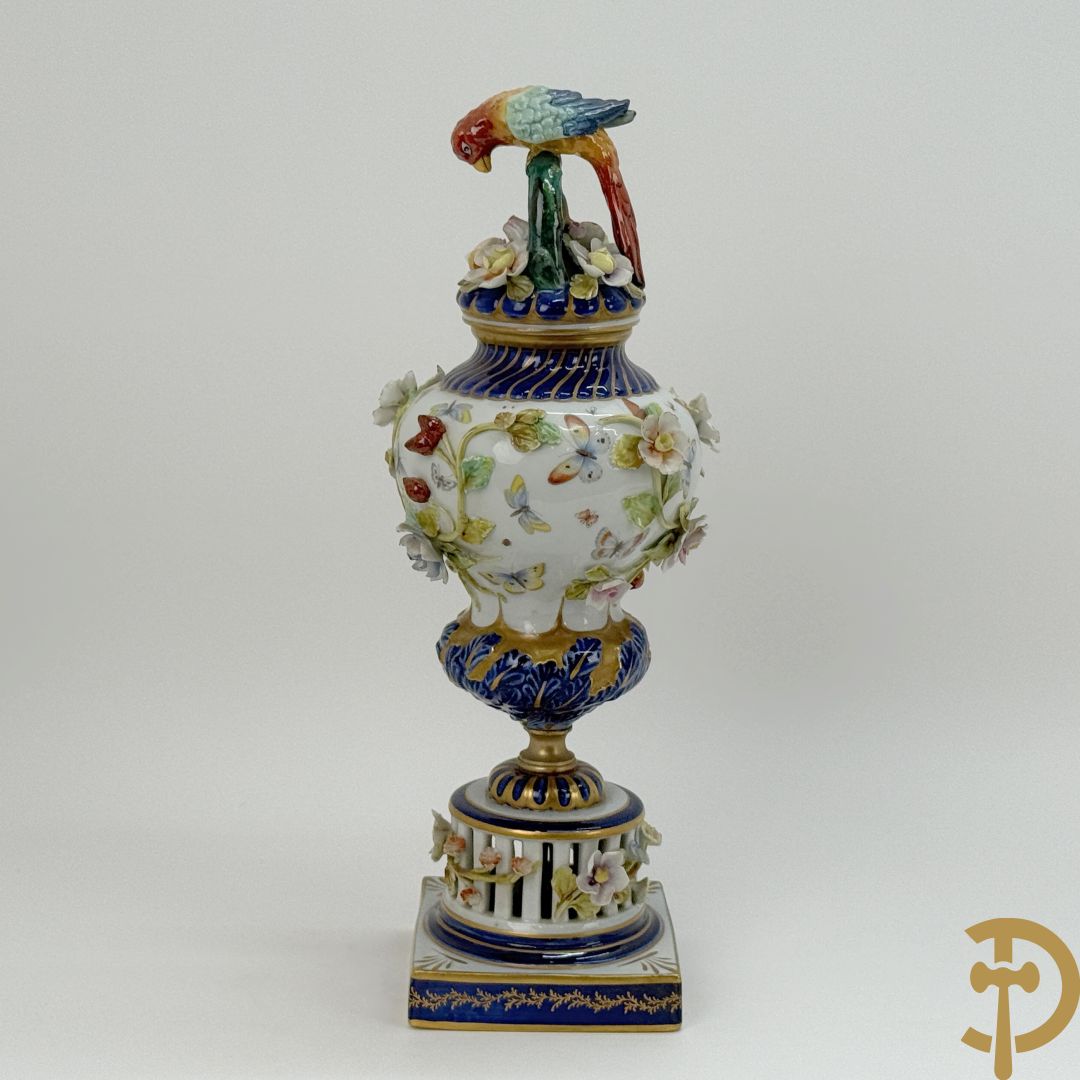 Porseleinen siervaas met handbeschilderd geanimeerd decor bezet met basrelief van bloemen en bovenaan bekroond met deksel met vogel