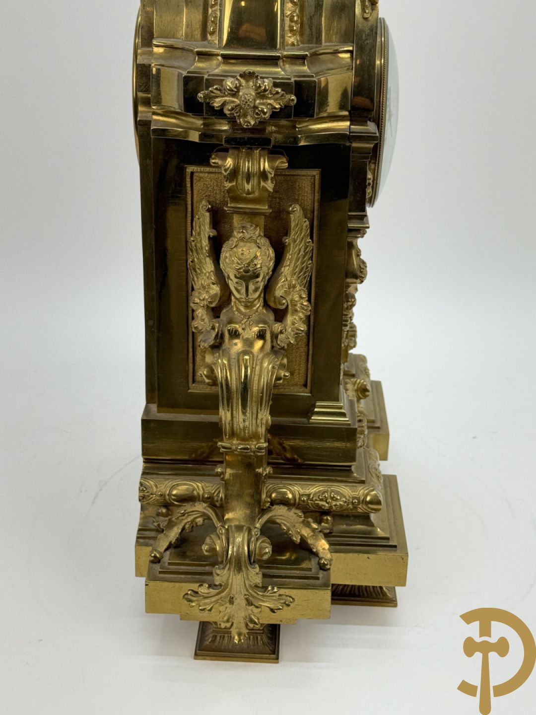 Vuurvergulde bronzen pendule, zijdelings bezet met gevleugelde dames, bovenaan met amfoor