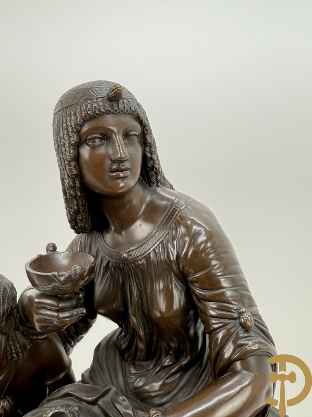 Driedelige bronzen garnituur bestaande uit middenstuk met bronzen vuurvergulde klok, Daubrée gemerkt à Nancy, bovenaan bekroond met Cleopatra met drinkbeker - getekend van Cumberworth sculpteur - geflankeerd door paar cupido