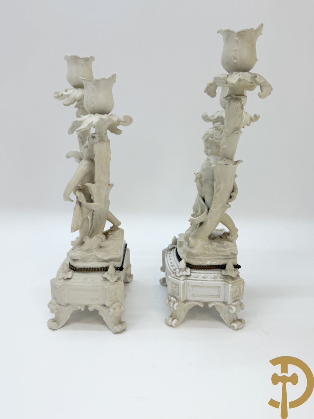 Driedelige porseleinen garnituur bestaande uit pendule bezet met lieftallig koppel, geflankeerd door paar kandelaars met cupido