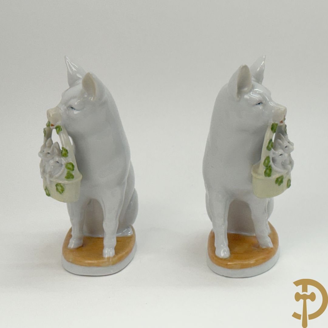 Koppel porseleinen beeldjes met varkens houdende een mandje met biggetjes