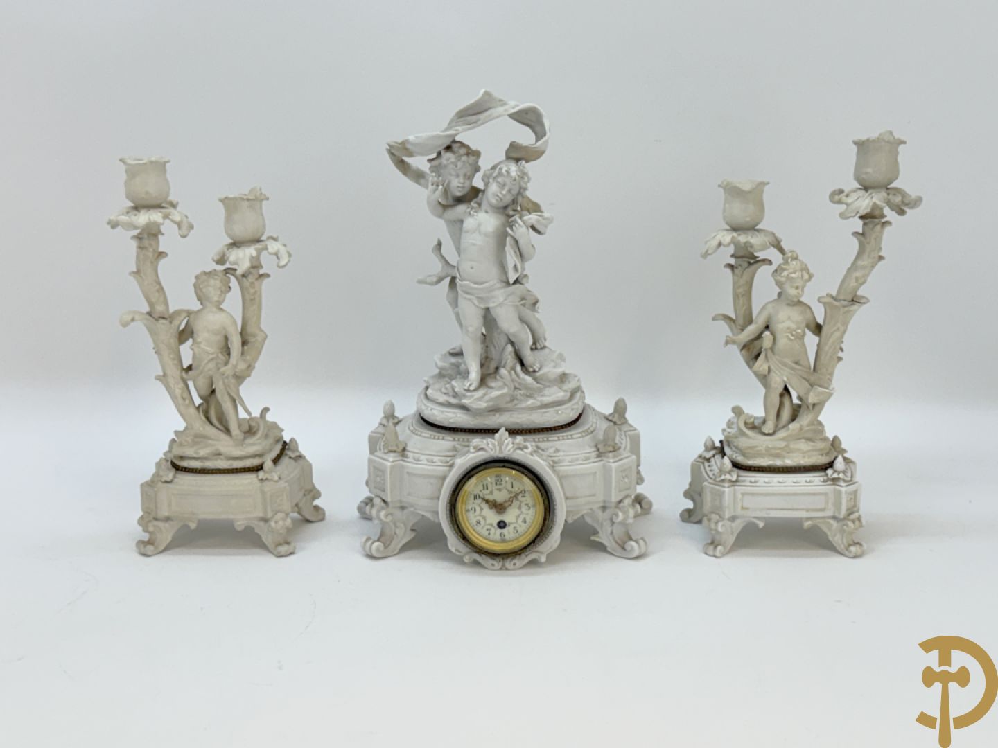 Driedelige porseleinen garnituur bestaande uit pendule bezet met lieftallig koppel, geflankeerd door paar kandelaars met cupido