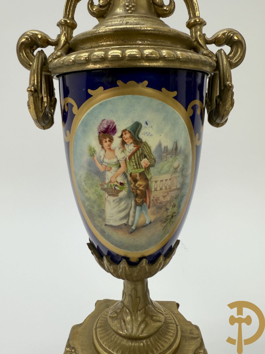 Driedelige koperen garnituur bestaande uit pendule met beschilderd romantisch tafereel en amfoor, zijdelings bezet met paar cassolettes met geanimeerde scènes, onleesbaar getekend rechts onder klok