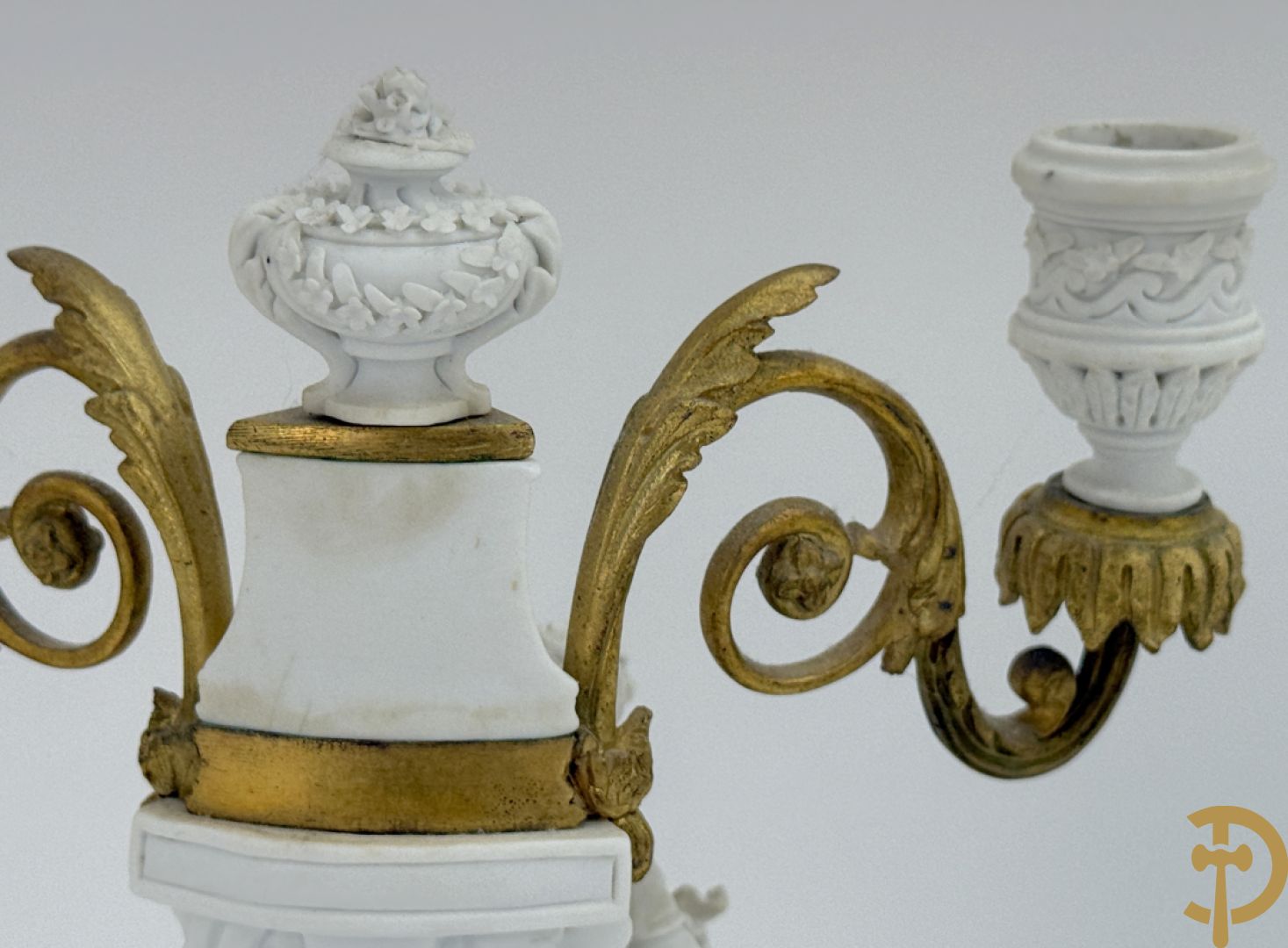 Driedelige porseleinen garnituur met bronsbeslag bestaande uit pendule met dame en amfoor geflankeerd door paar kandelaars bezet met personages