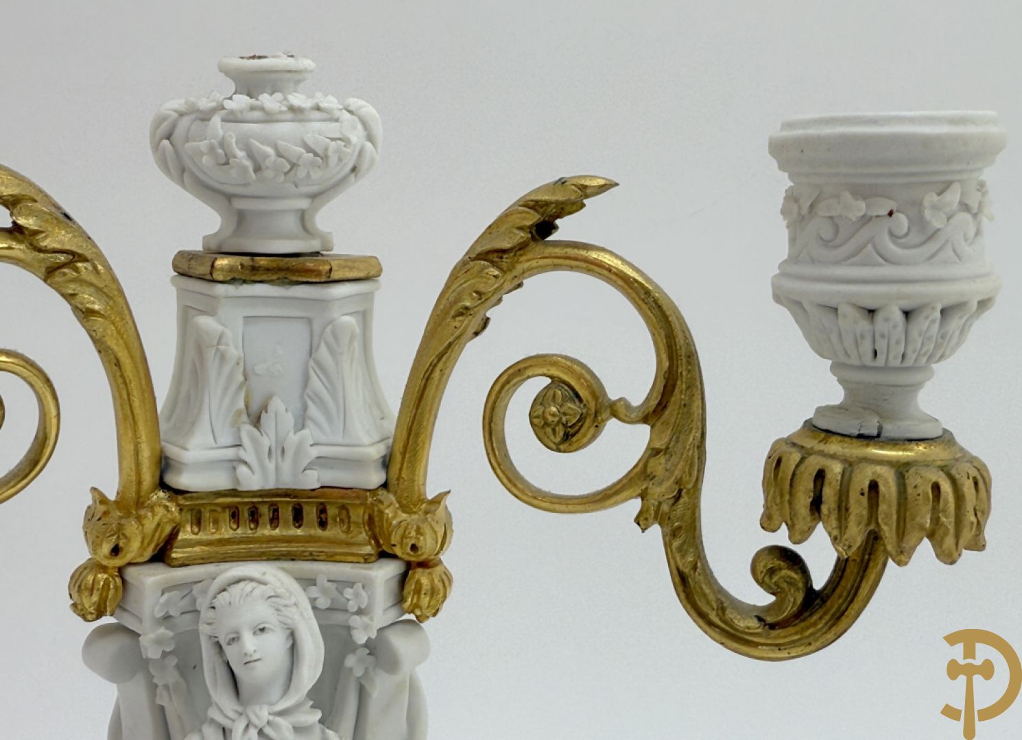 Driedelige porseleinen garnituur met bronsbeslag bestaande uit pendule met dame en amfoor geflankeerd door paar kandelaars bezet met personages