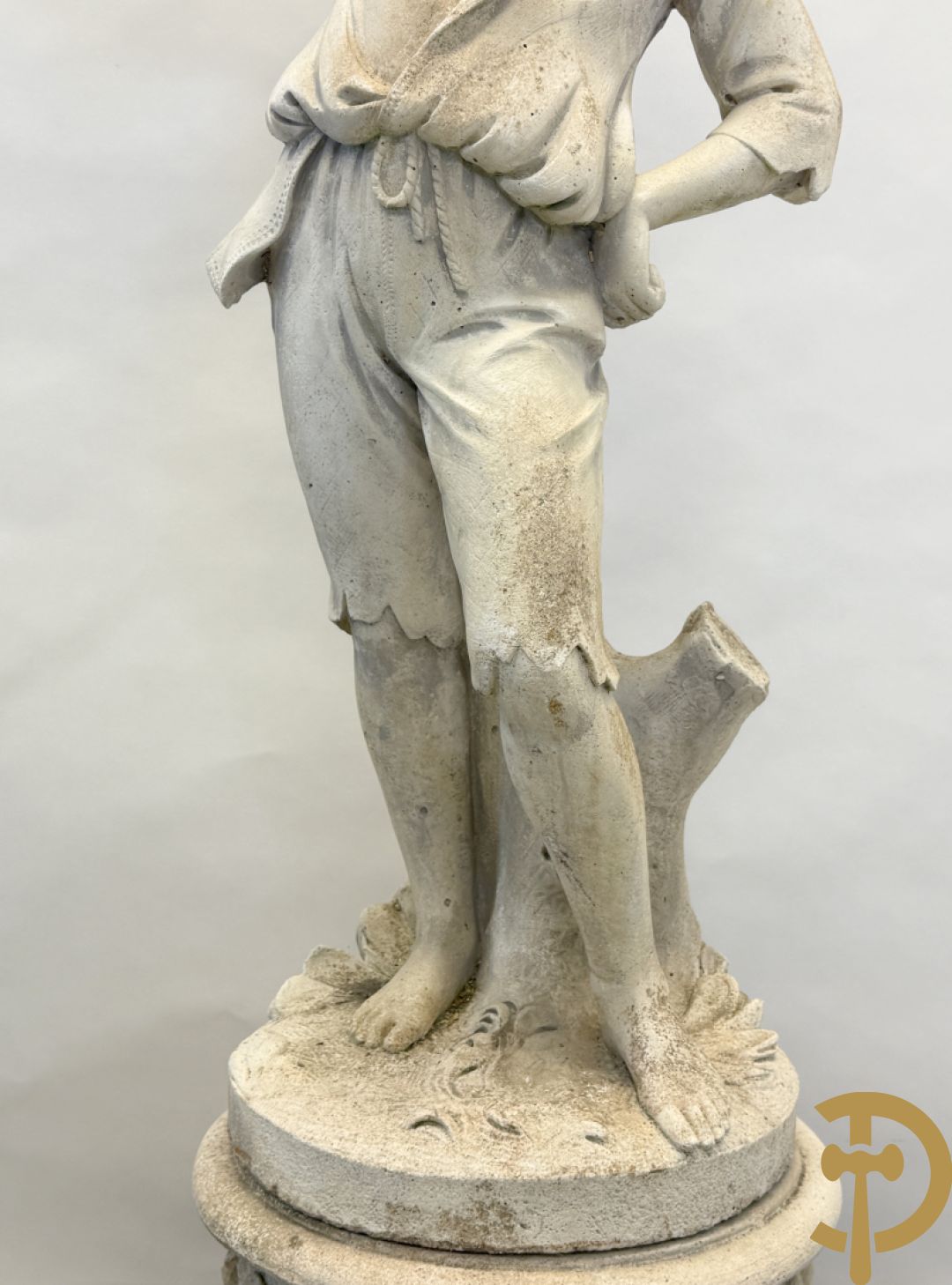 Stenen tuinbeeld van jongeman met mand in de hand op sokkel met guirlandes