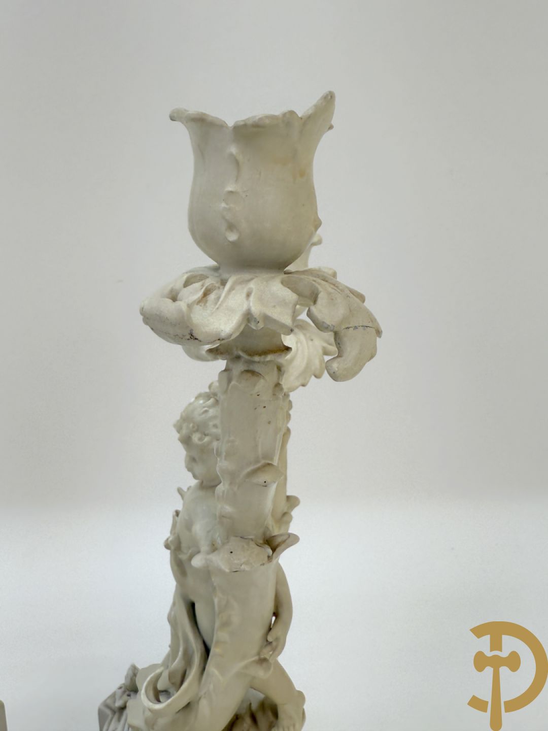 Driedelige porseleinen garnituur bestaande uit pendule bezet met lieftallig koppel, geflankeerd door paar kandelaars met cupido