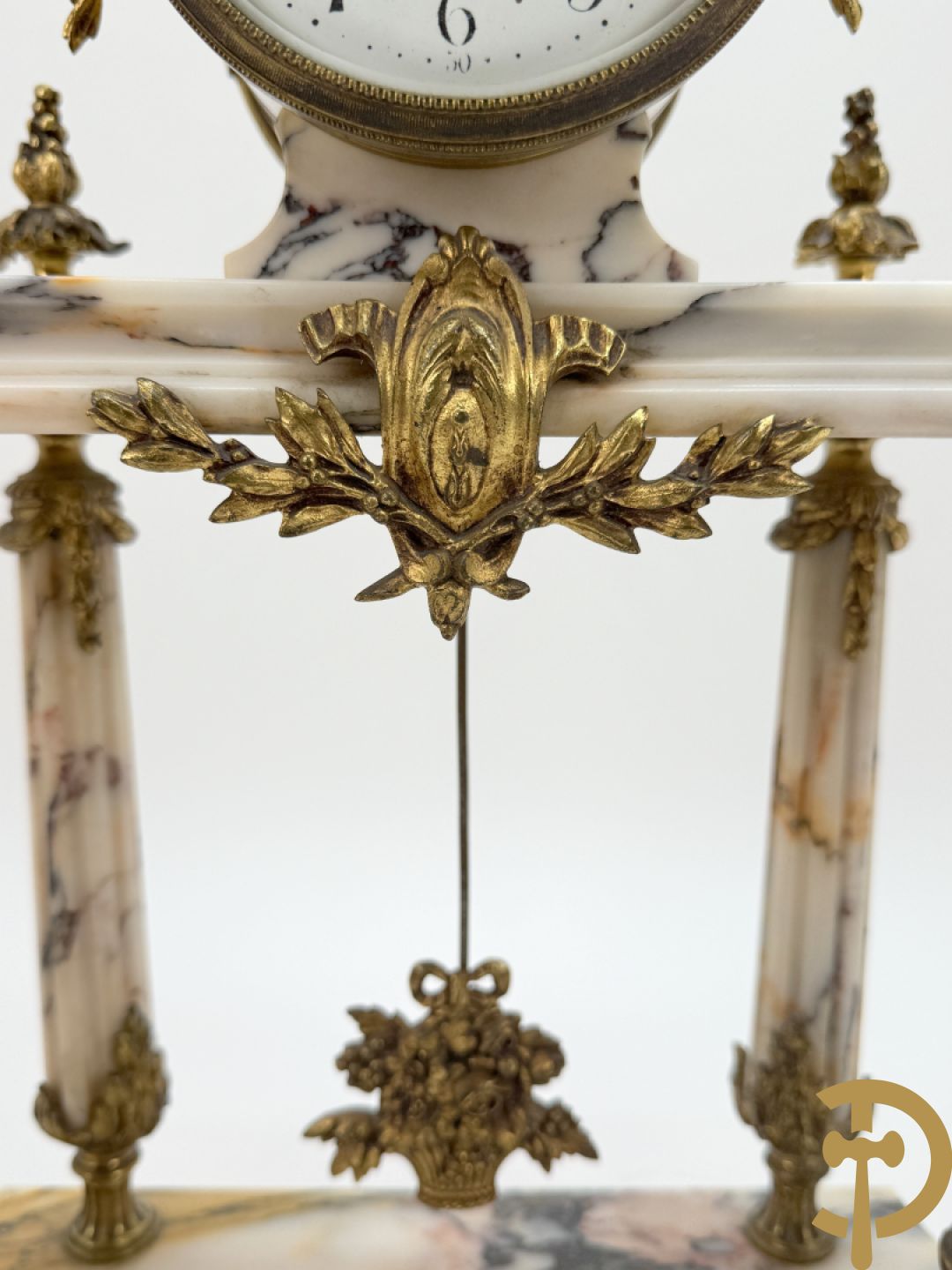 Driedelige wit marmeren garnituur bestaande uit vierzuilenpendule met bloemen en troffee geflankeerd door paar cassolettes met ramskoppen bezet