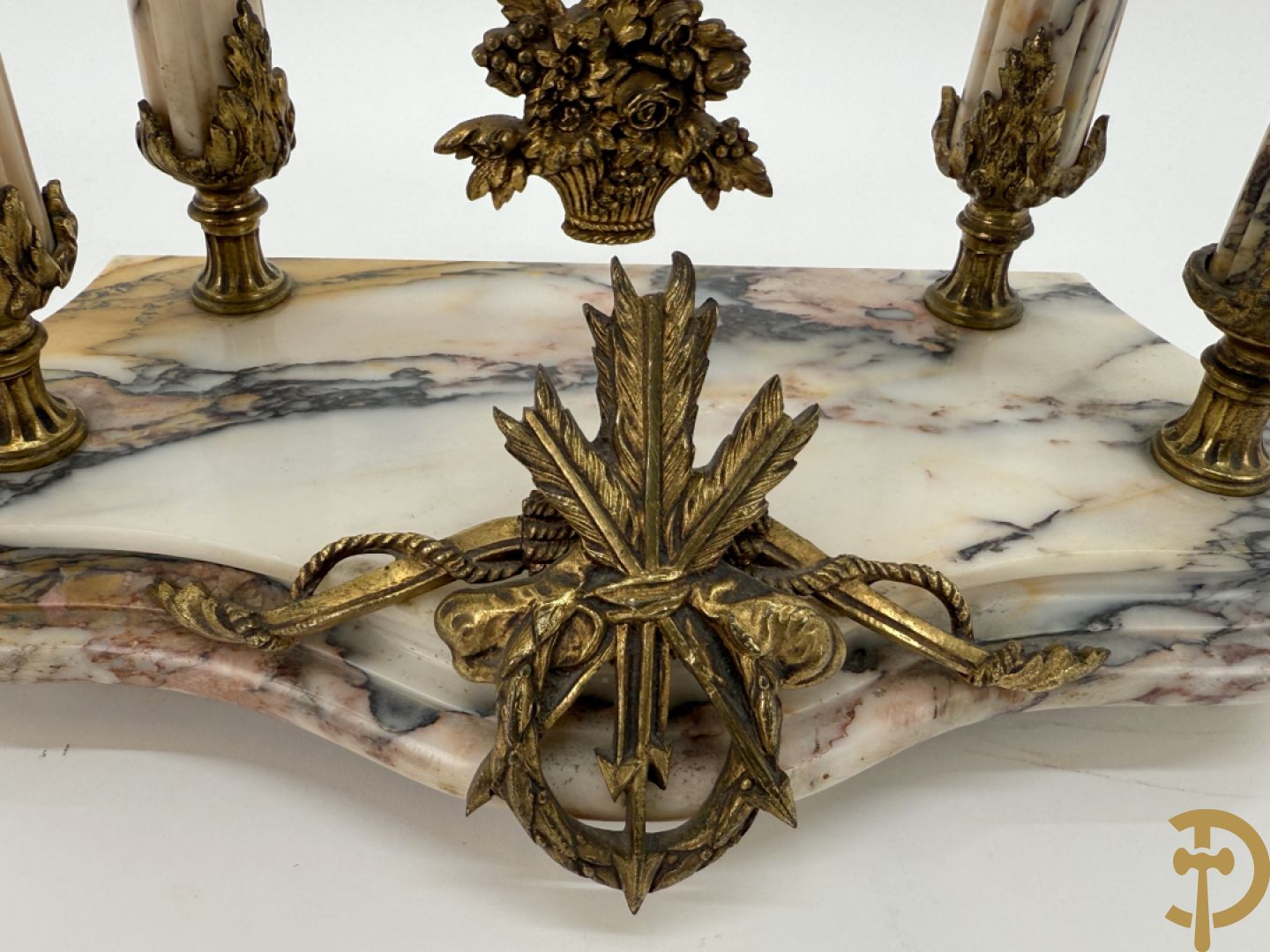 Driedelige wit marmeren garnituur bestaande uit vierzuilenpendule met bloemen en troffee geflankeerd door paar cassolettes met ramskoppen bezet