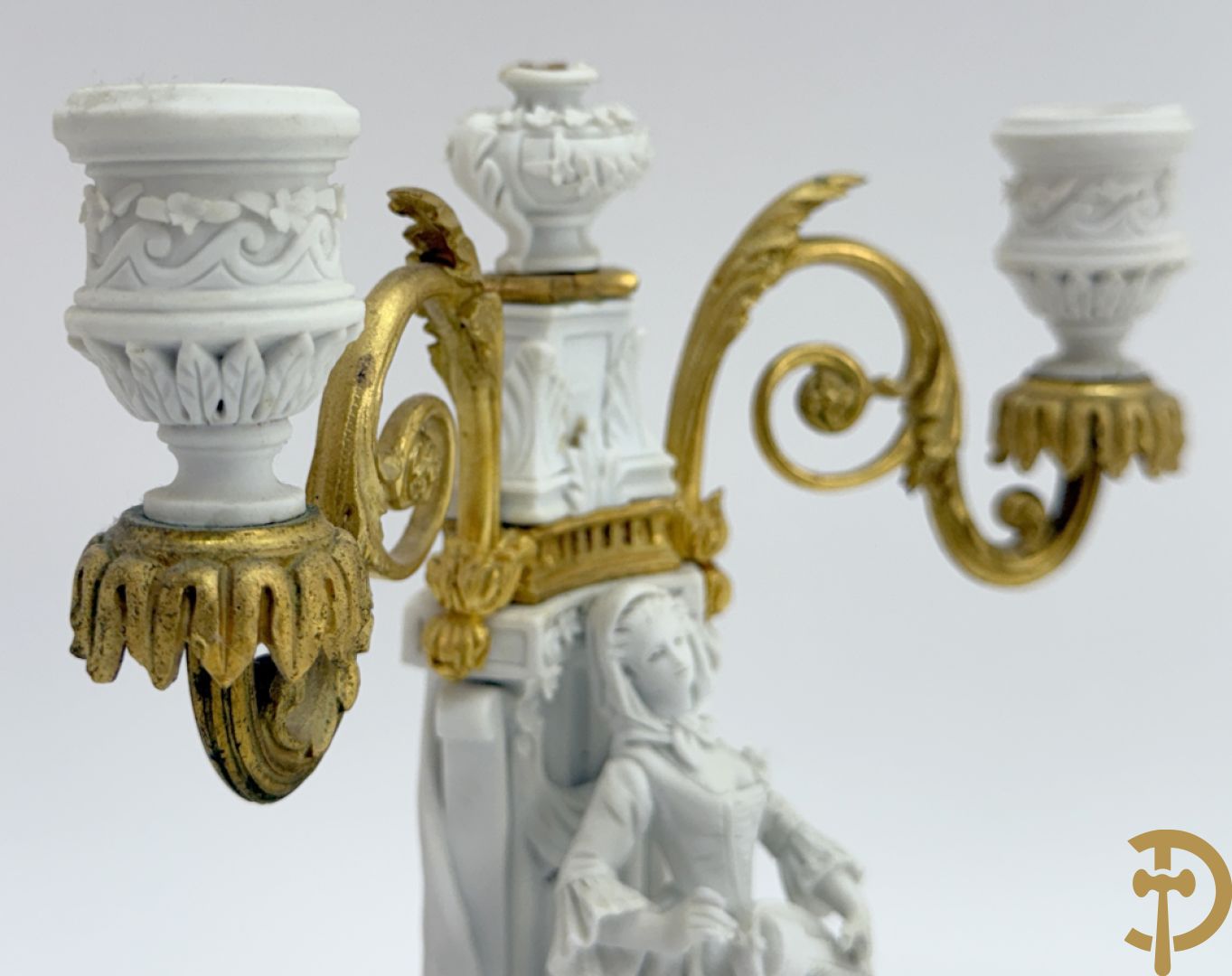 Driedelige porseleinen garnituur met bronsbeslag bestaande uit pendule met dame en amfoor geflankeerd door paar kandelaars bezet met personages