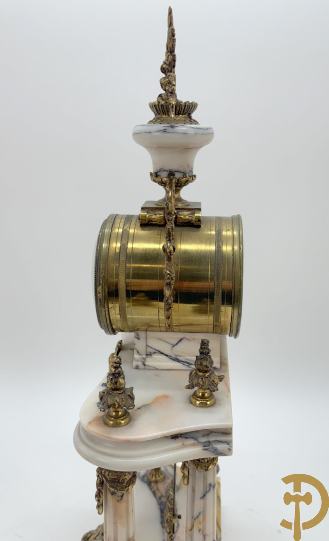 Driedelige wit marmeren garnituur bestaande uit vierzuilenpendule met bloemen en troffee geflankeerd door paar cassolettes met ramskoppen bezet