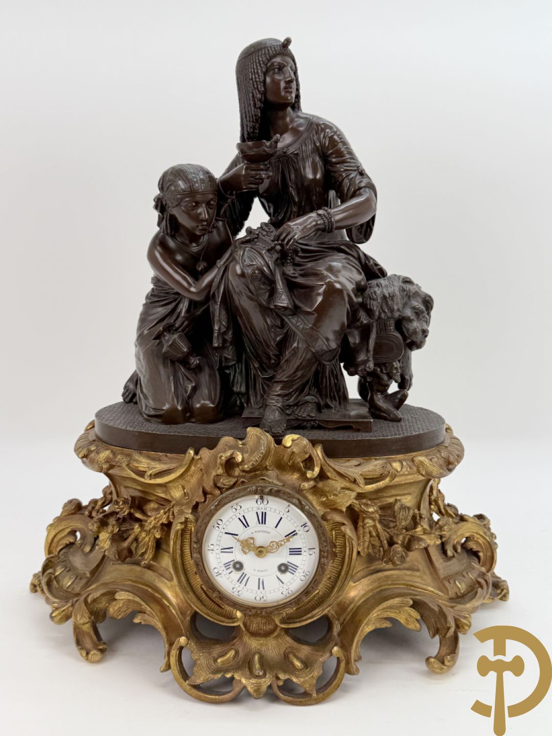 Driedelige bronzen garnituur bestaande uit middenstuk met bronzen vuurvergulde klok, Daubrée gemerkt à Nancy, bovenaan bekroond met Cleopatra met drinkbeker - getekend van Cumberworth sculpteur - geflankeerd door paar cupido