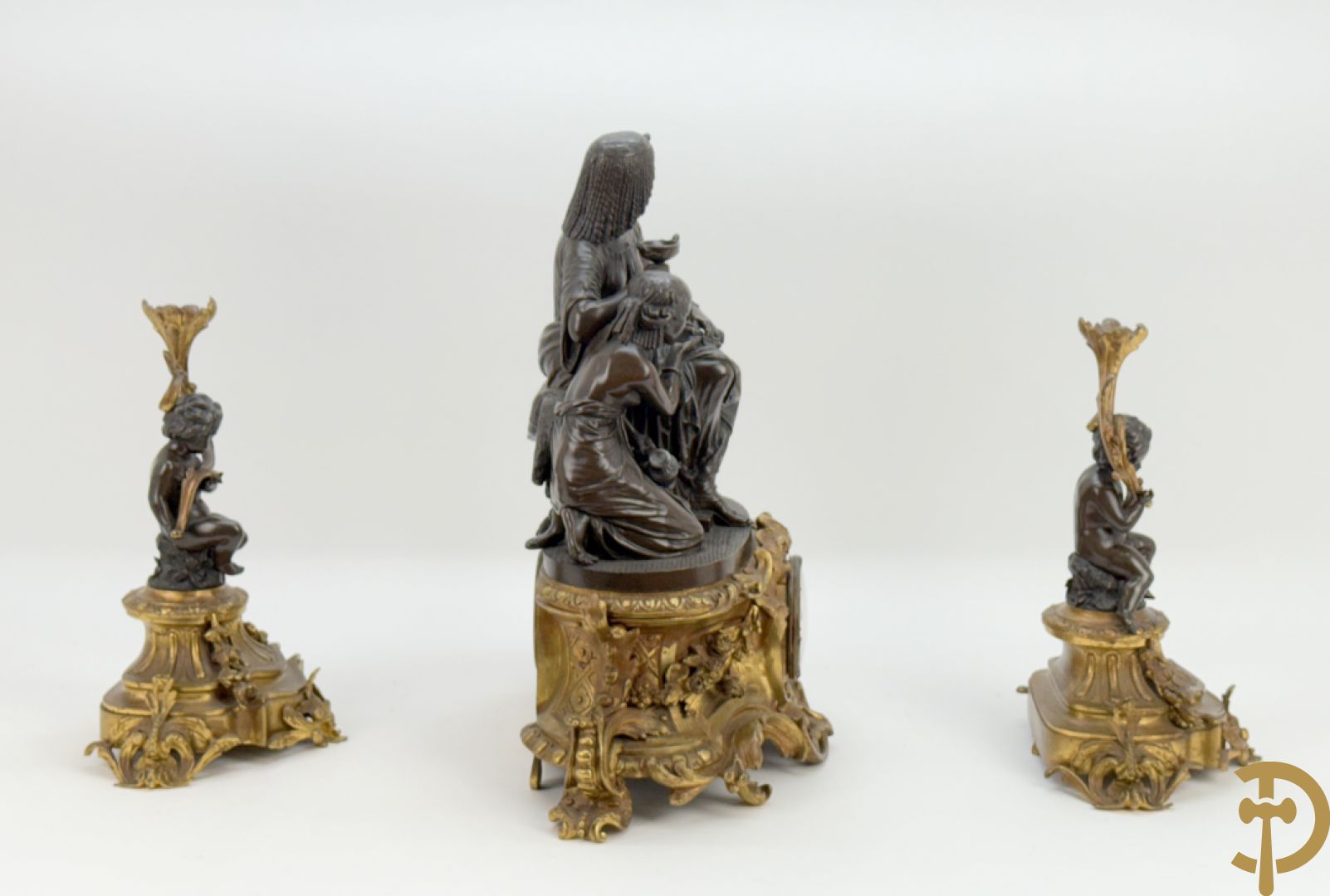 Driedelige bronzen garnituur bestaande uit middenstuk met bronzen vuurvergulde klok, Daubrée gemerkt à Nancy, bovenaan bekroond met Cleopatra met drinkbeker - getekend van Cumberworth sculpteur - geflankeerd door paar cupido