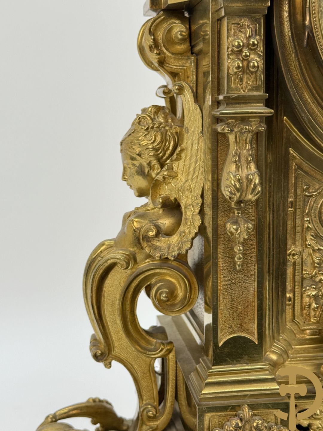 Vuurvergulde bronzen pendule, zijdelings bezet met gevleugelde dames, bovenaan met amfoor