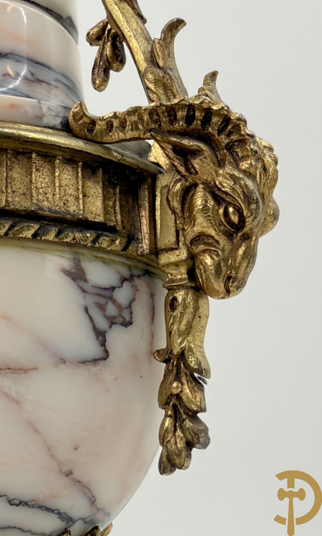 Driedelige wit marmeren garnituur bestaande uit vierzuilenpendule met bloemen en troffee geflankeerd door paar cassolettes met ramskoppen bezet