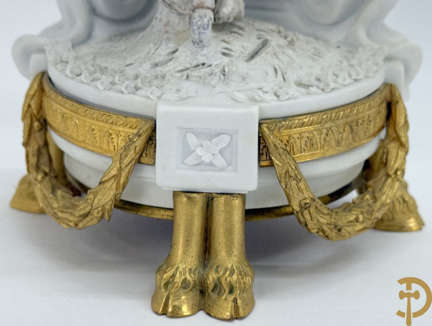 Driedelige porseleinen garnituur met bronsbeslag bestaande uit pendule met dame en amfoor geflankeerd door paar kandelaars bezet met personages