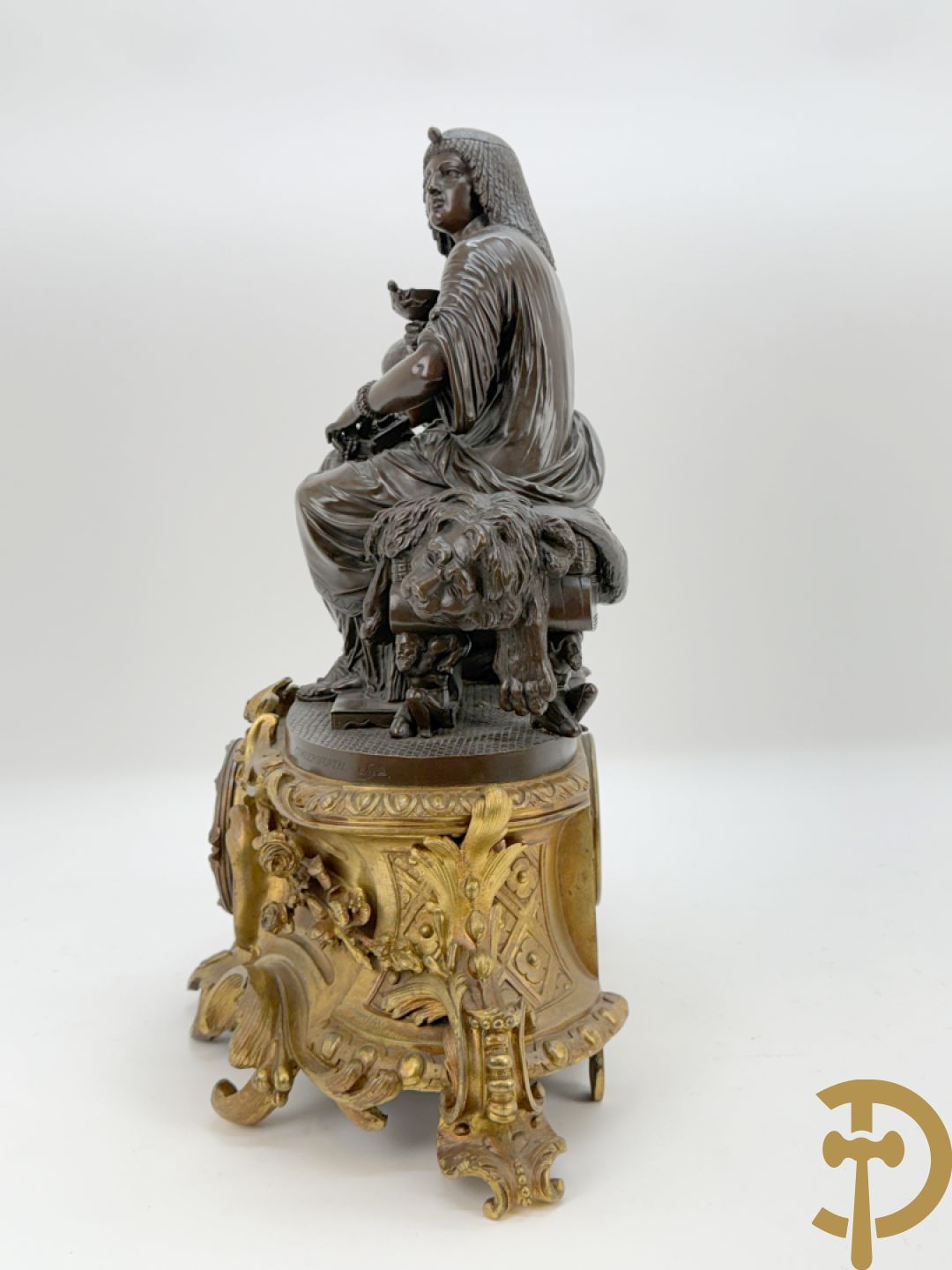 Driedelige bronzen garnituur bestaande uit middenstuk met bronzen vuurvergulde klok, Daubrée gemerkt à Nancy, bovenaan bekroond met Cleopatra met drinkbeker - getekend van Cumberworth sculpteur - geflankeerd door paar cupido