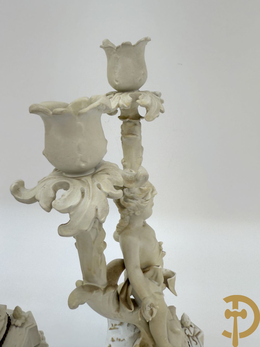 Driedelige porseleinen garnituur bestaande uit pendule bezet met lieftallig koppel, geflankeerd door paar kandelaars met cupido