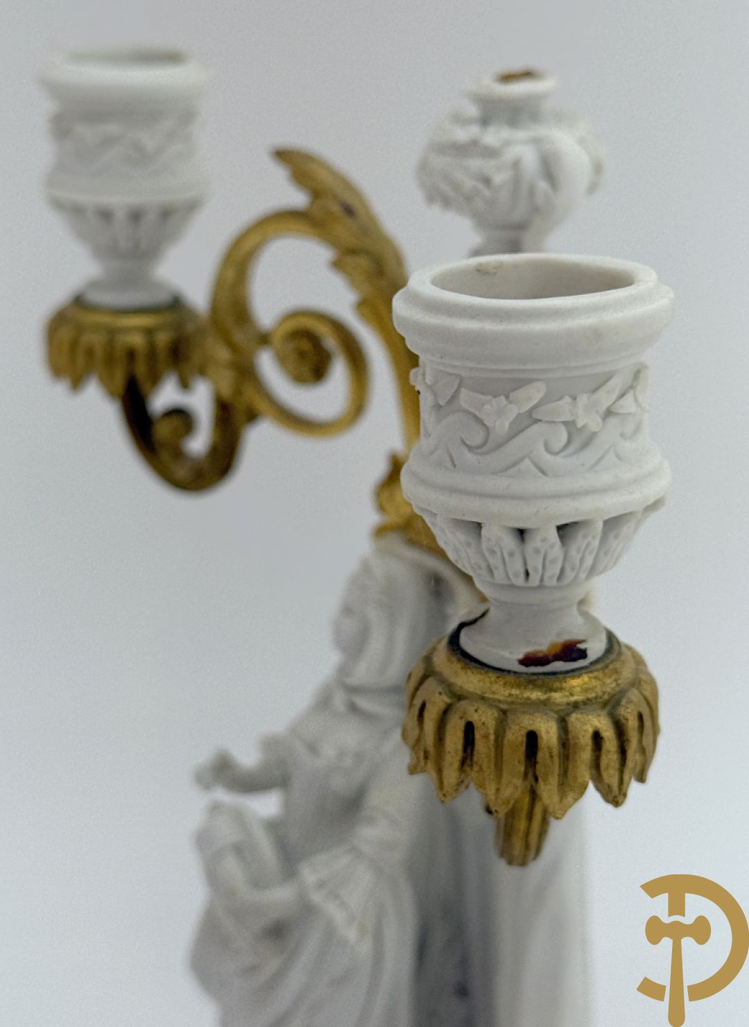 Driedelige porseleinen garnituur met bronsbeslag bestaande uit pendule met dame en amfoor geflankeerd door paar kandelaars bezet met personages